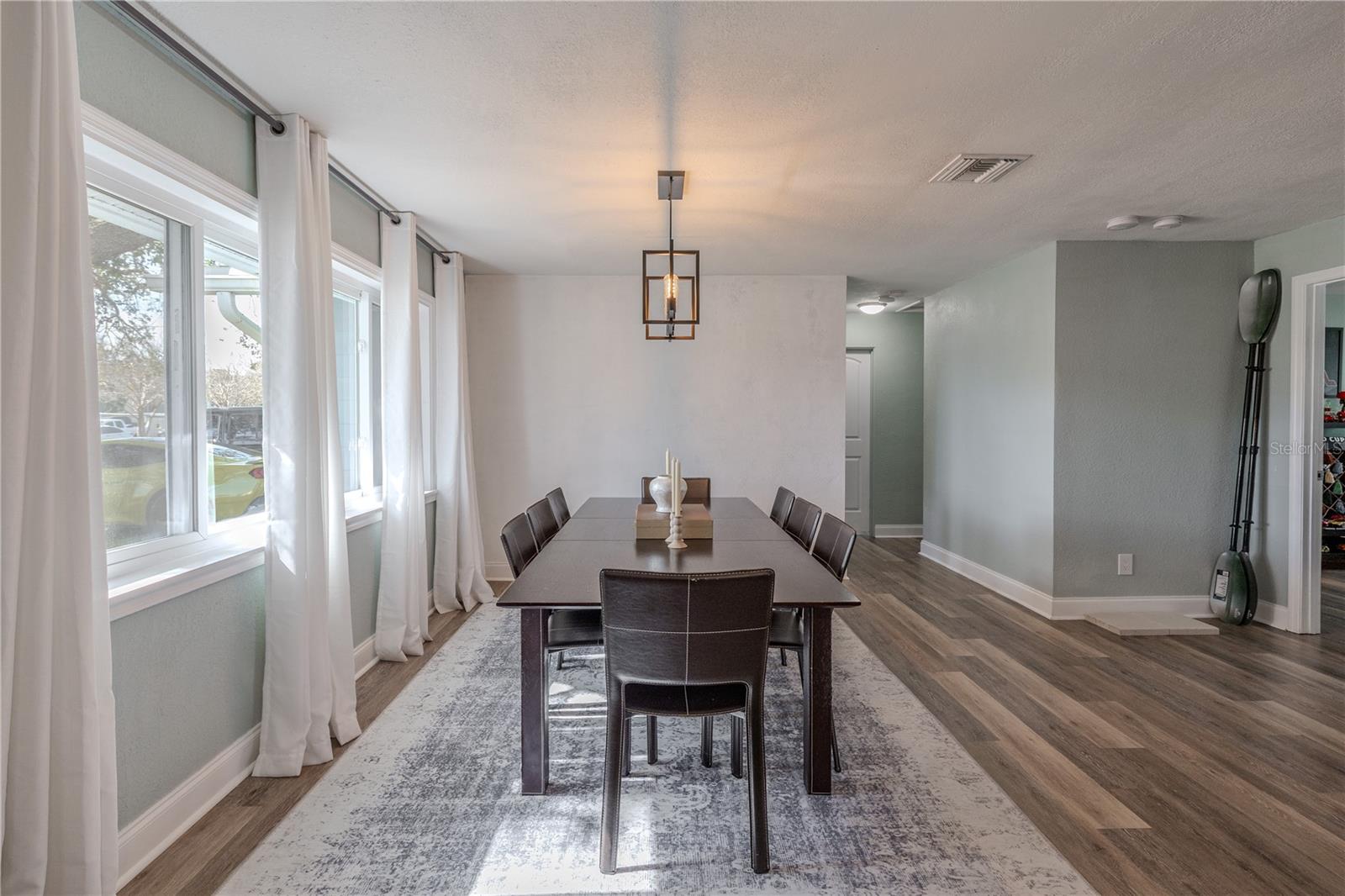 Light-filled dining area features wide-plank vinyl flooring, a modern pendant light, and a wall of windows with flowing drapery—perfect for hosting family and friends.