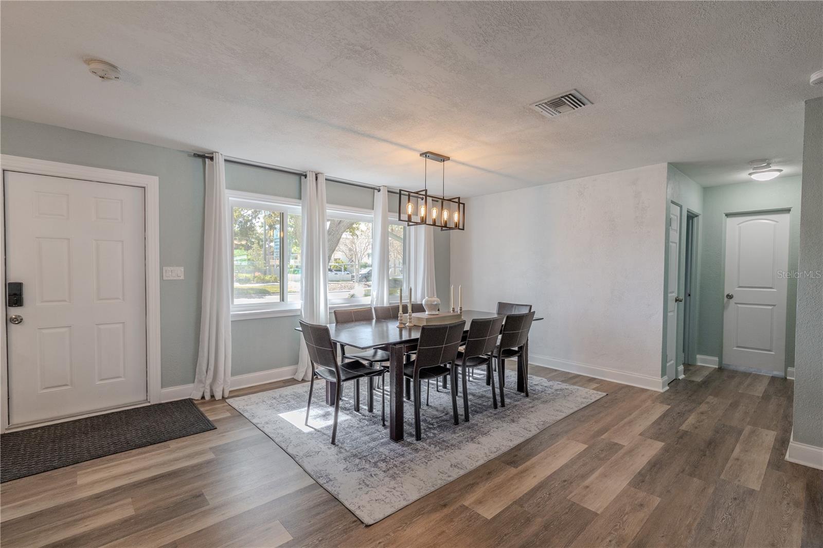 Inviting dining space features wide-plank vinyl flooring, a modern chandelier, and bright windows with flowing curtains, plus an easy flow to the kitchen and living areas.