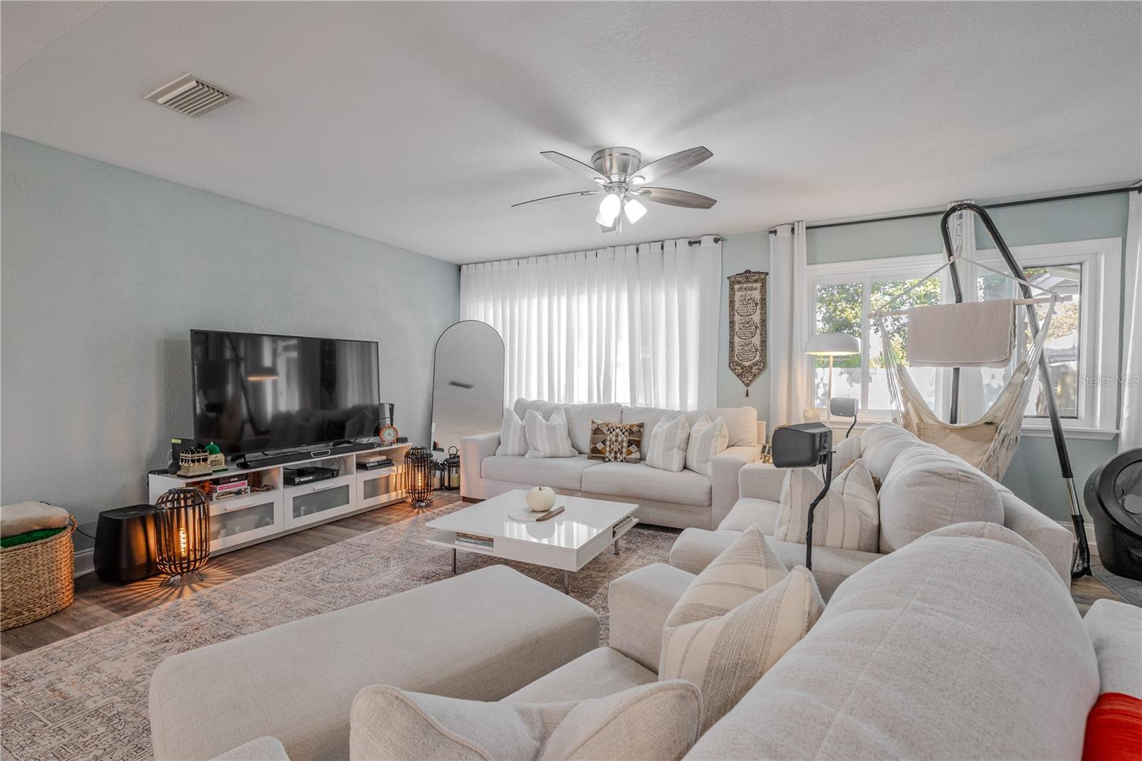 Inviting living room features wide-plank vinyl flooring, a modern ceiling fan, and oversized windows that fill the space with natural light for a bright, comfortable gathering area.