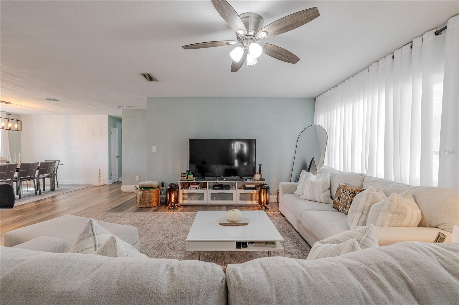 Spacious living room is filled with natural light and features wide-plank vinyl flooring, a modern ceiling fan, and an open layout that flows seamlessly to the dining area.