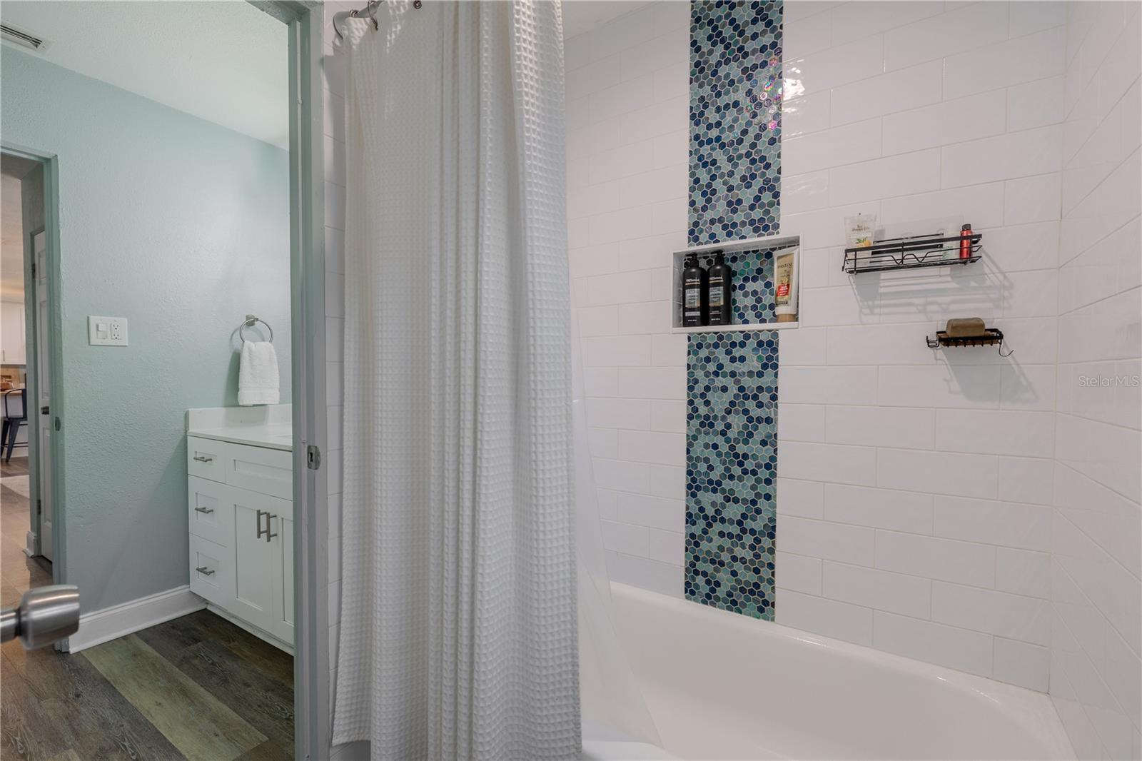 Fresh tub/shower combo features crisp subway tile, a stylish mosaic accent strip, and a built-in niche for convenient storage.