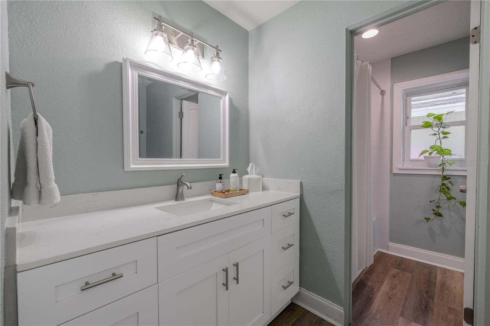 Bright bathroom features a sleek white vanity with ample storage, bright lighting, and a tub/shower area with a window for natural light.