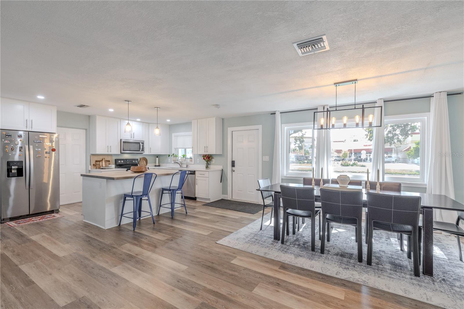 Stylish open-concept kitchen and dining area features white cabinetry, wide-plank vinyl flooring, a spacious breakfast bar, and a bright dining space with modern lighting.