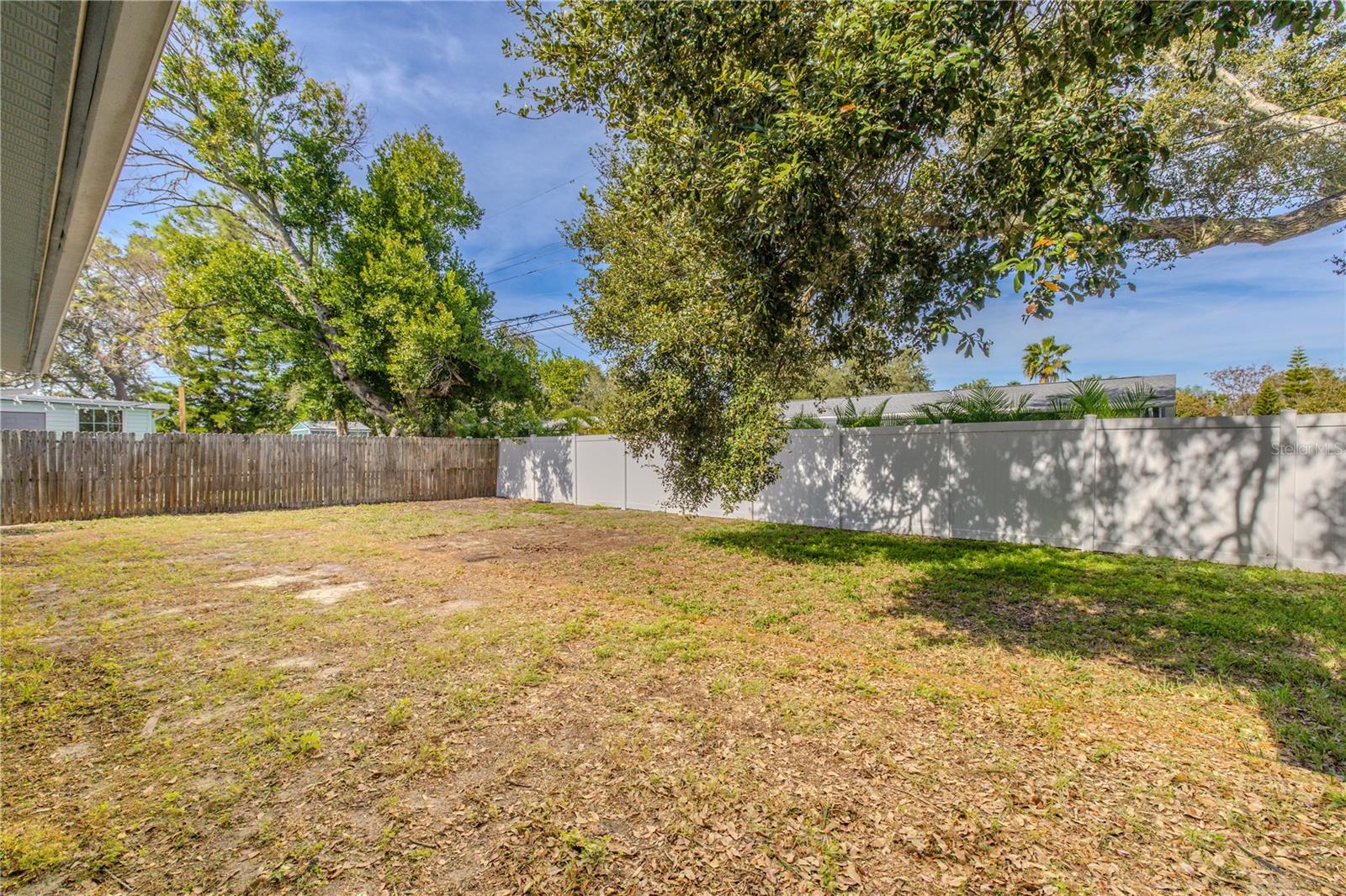 Additional view of the partially fenced backyard provides a wide open lawn with mature shade trees and easy access to the screened patio—perfect for play, and outdoor entertaining.