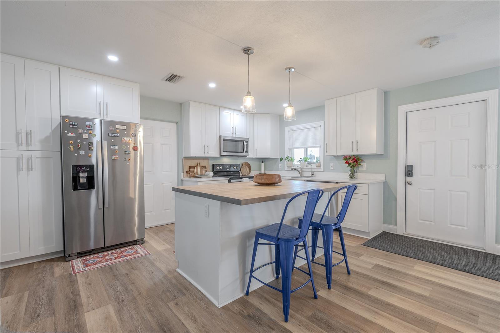 Beautifully designed kitchen features crisp white cabinetry, stainless appliances, and a large center island with pendant lighting and seating, all atop wide-plank vinyl flooring.