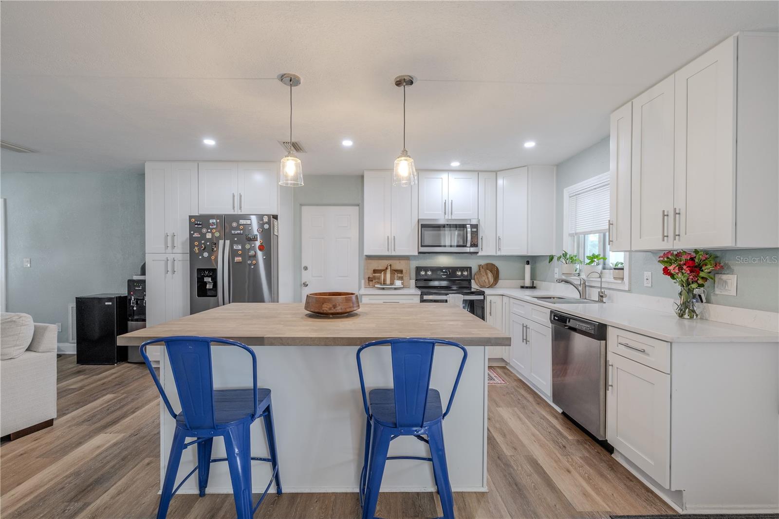 Sleek modern kitchen features abundant white cabinetry, stainless appliances, and a large center island with pendant lighting and seating—perfect for gathering and entertaining.