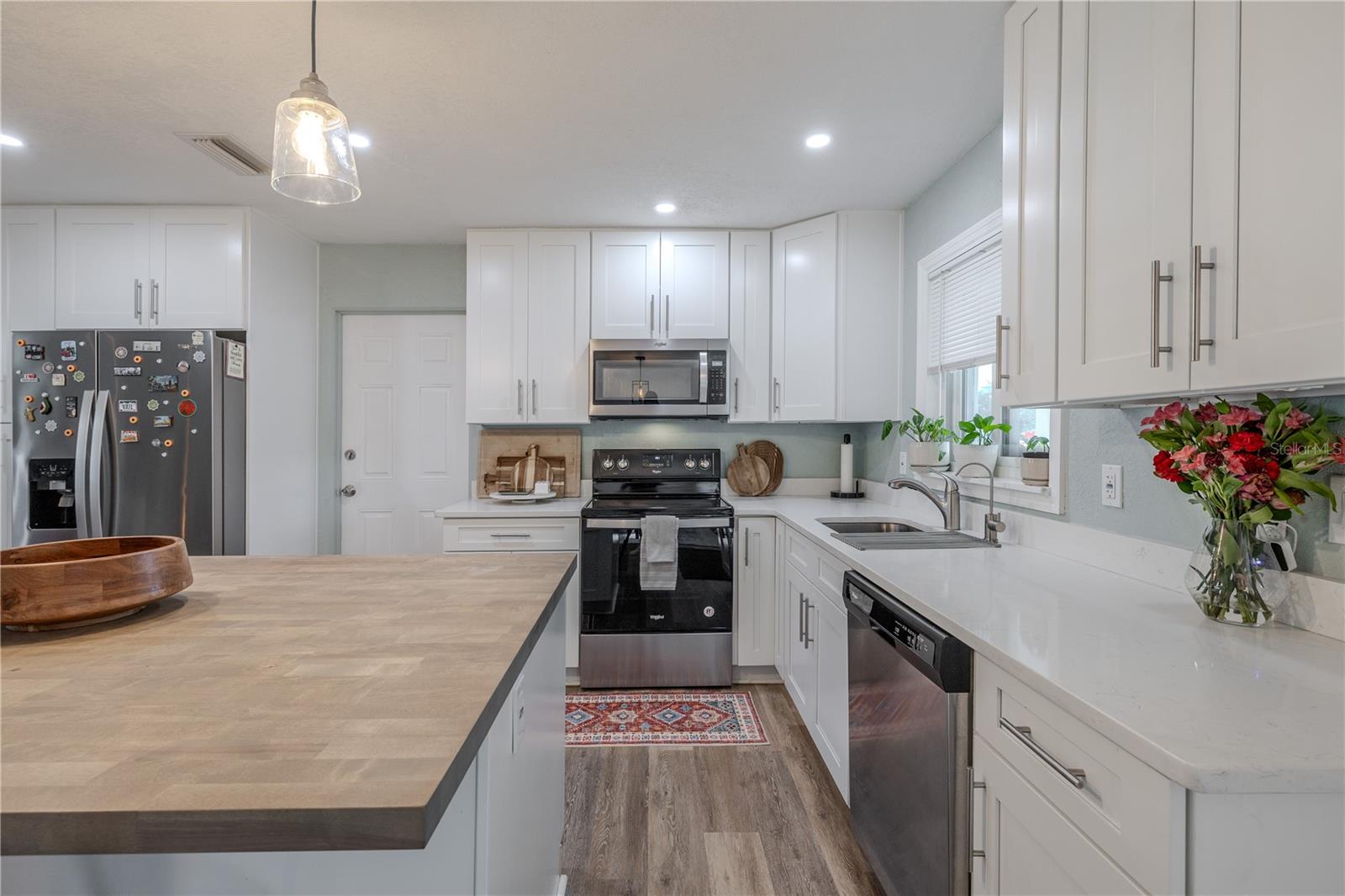 Bright kitchen showcases sleek white cabinetry, stainless appliances, quartz-style counters, and a large island—brightly lit with recessed and pendant lighting for a modern, airy feel.