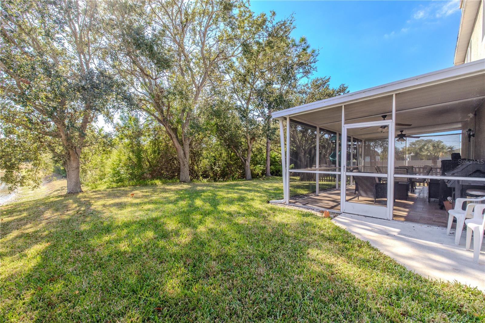 Enjoy a spacious backyard with mature shade trees and a screened lanai, offering a peaceful outdoor retreat with room to relax, play, or entertain.