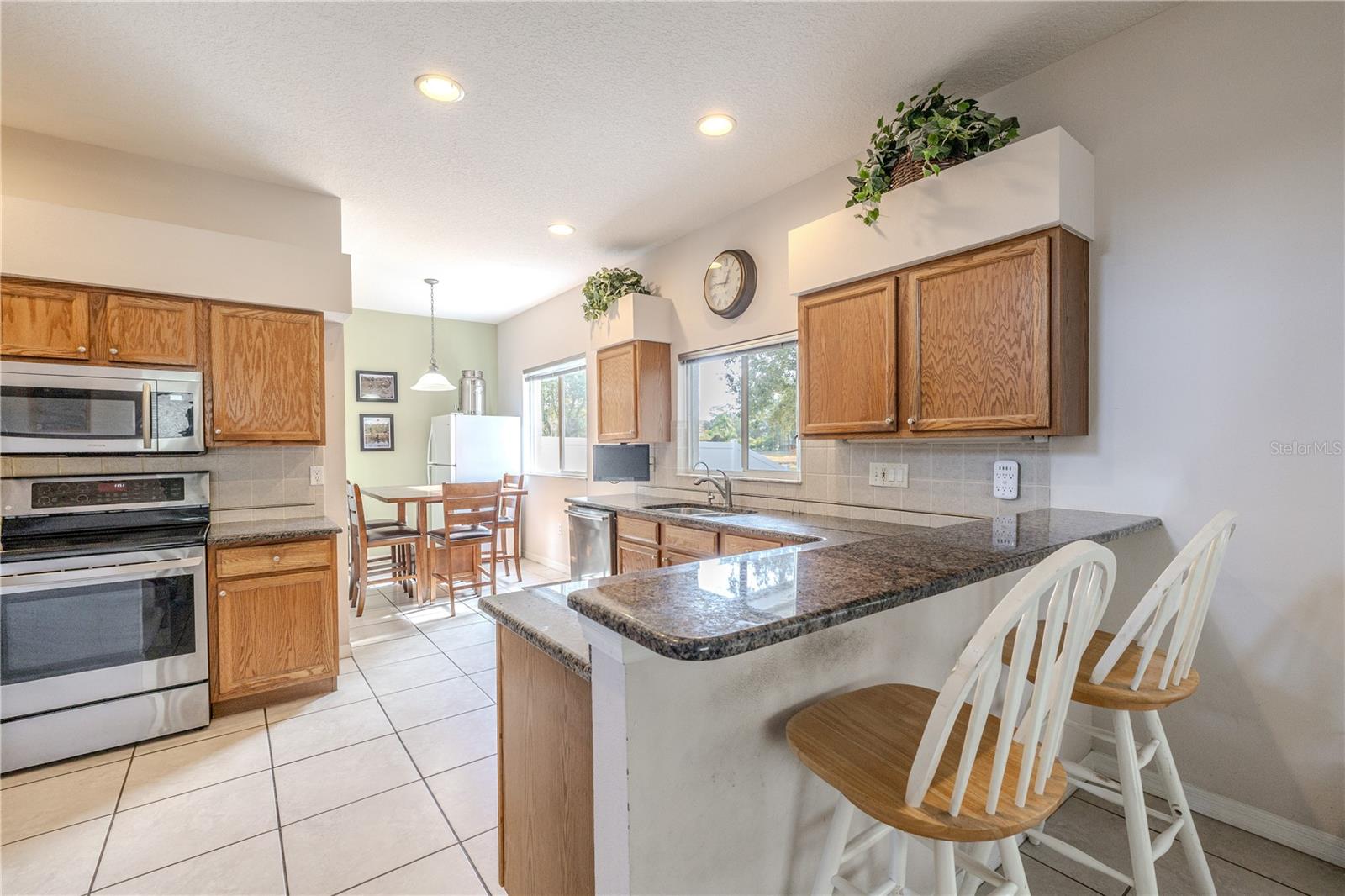 Bright eat-in kitchen features warm wood cabinetry, granite countertops with breakfast bar seating, stainless appliances, and a sunny dinette area with backyard and pond views.