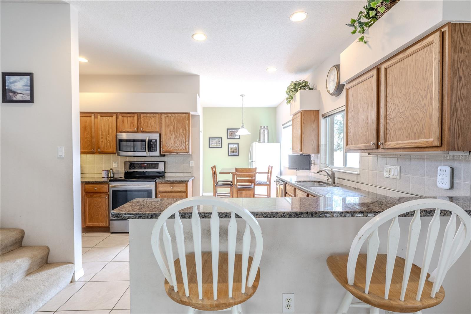 Open and airy kitchen offers granite breakfast-bar seating, abundant wood cabinetry, dual sinks, stainless appliances, and a bright breakfast nook area just beyond for casual meals.
