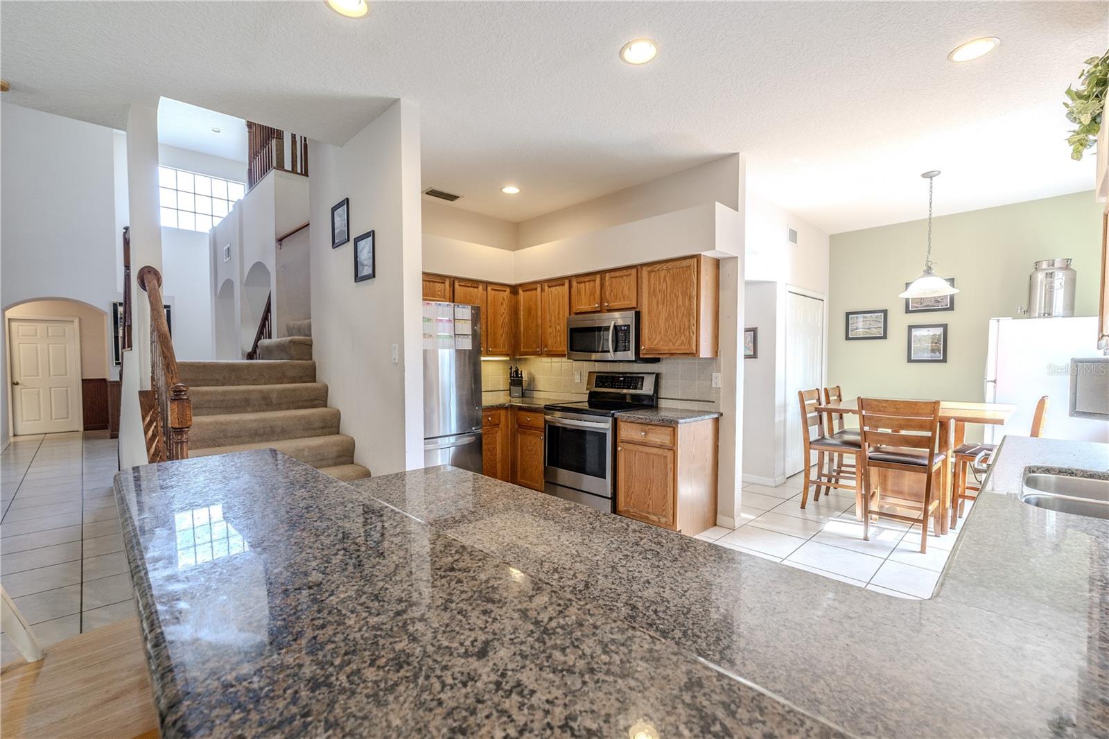 Spacious open kitchen features granite countertops, stainless appliances, and warm wood cabinetry, flowing into a sunny breakfast nook and the main living areas.