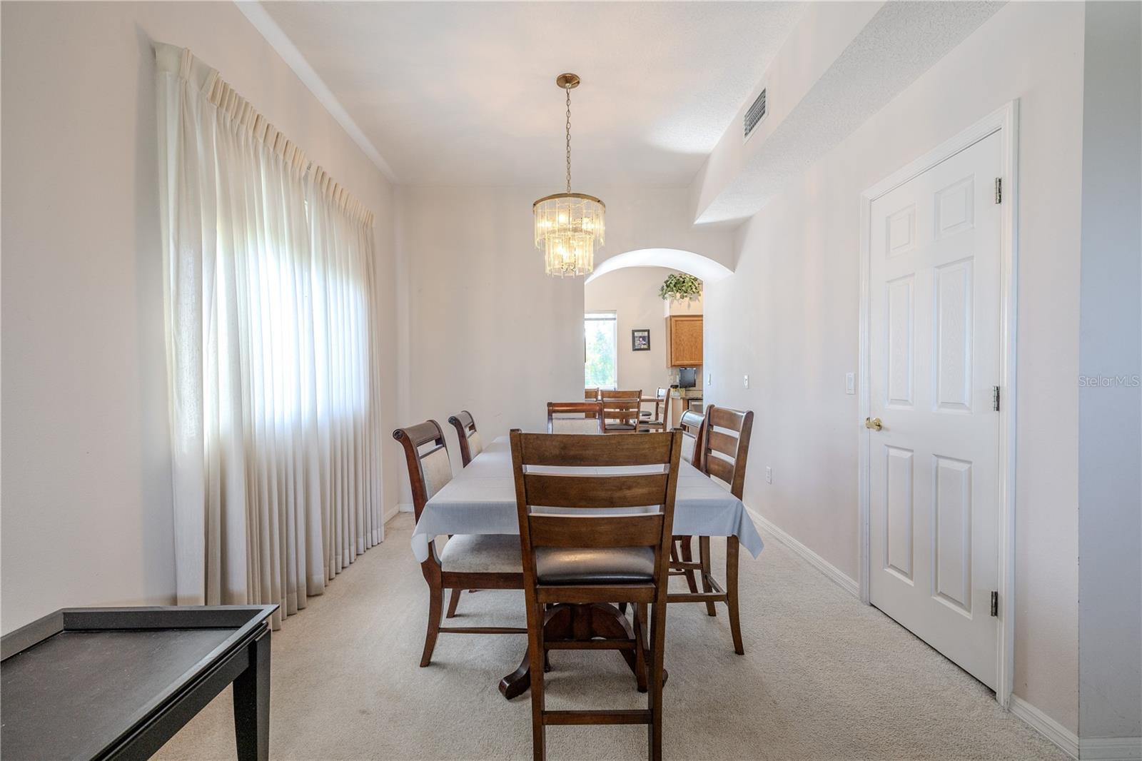 Formal dining room offers an inviting space with a sparkling chandelier, oversized window with soft drapes, large storage closet, and easy flow to the kitchen for effortless entertaining.