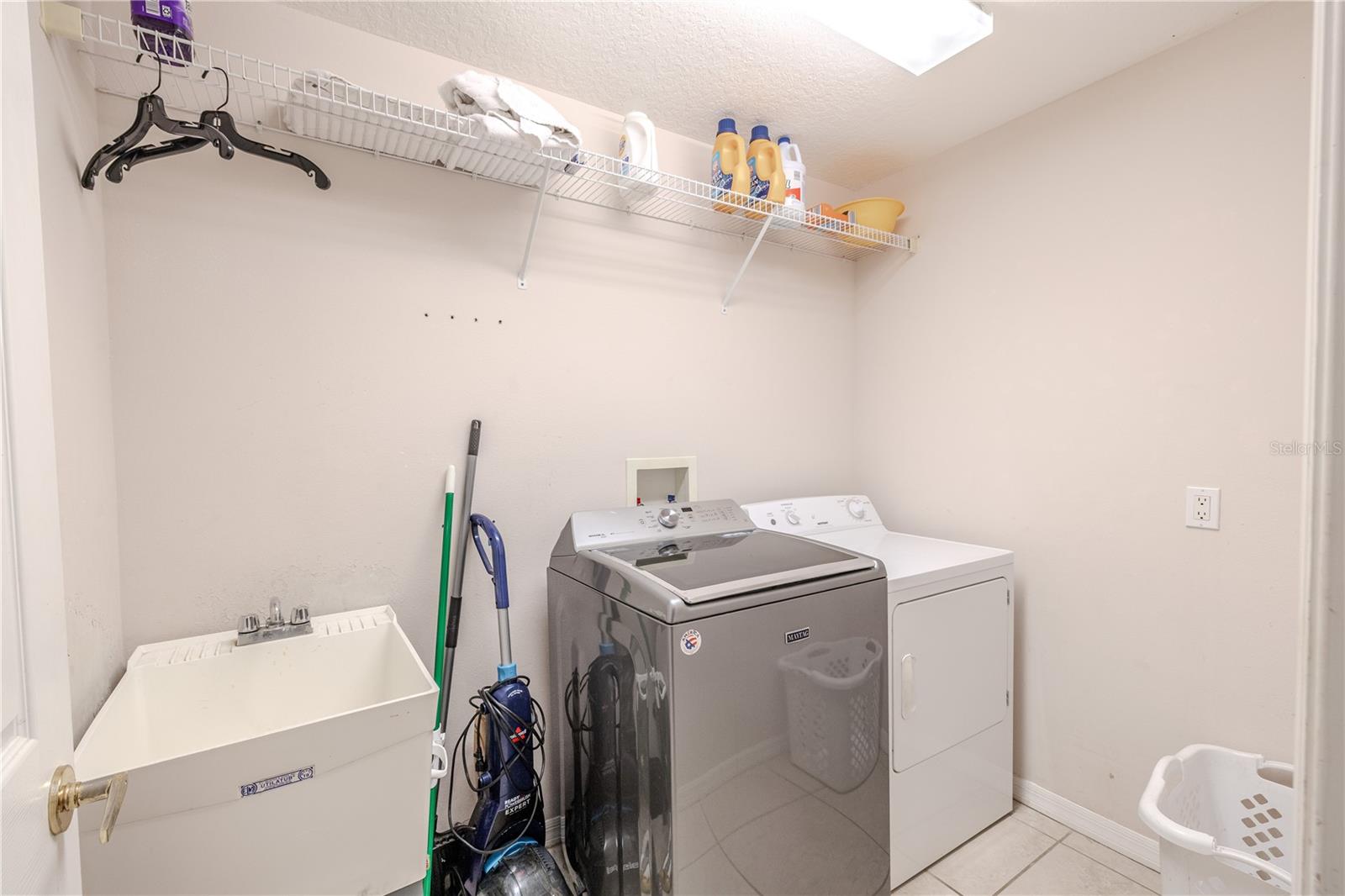 Dedicated laundry room features full-size washer and dryer, utility sink, and convenient shelving for added storage and organization.