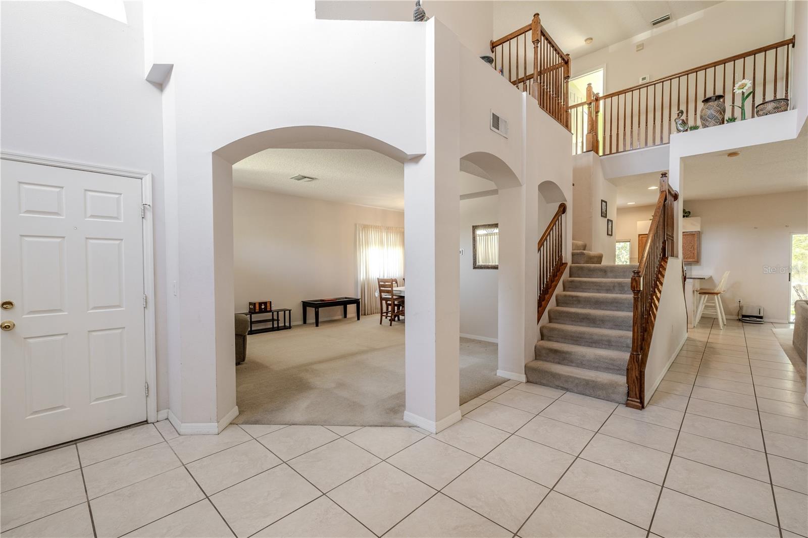 Grand two-story foyer showcases an open layout with tile flooring, arched entryways, and a sweeping staircase with warm wood railings that creates an impressive first impression.