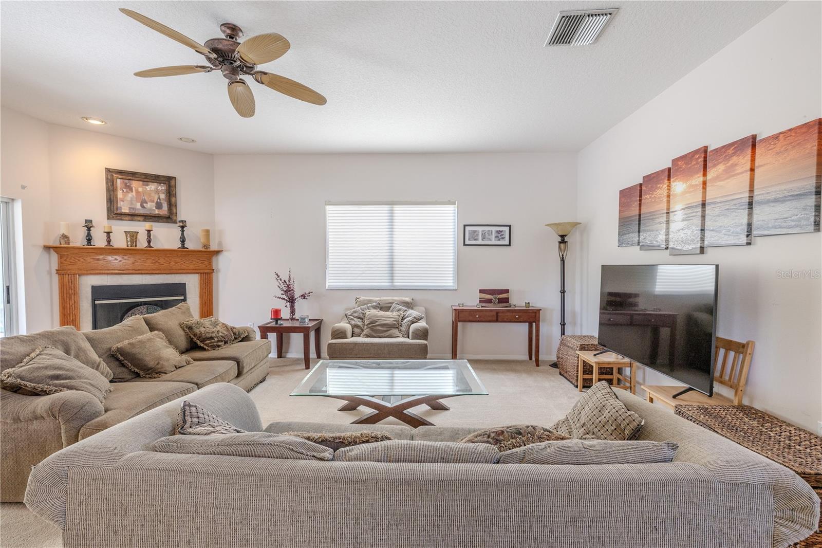 Spacious carpeted family room offers a warm, inviting atmosphere with plush seating, a classic wood-mantle fireplace, and plenty of natural light—perfect for relaxing or entertaining.