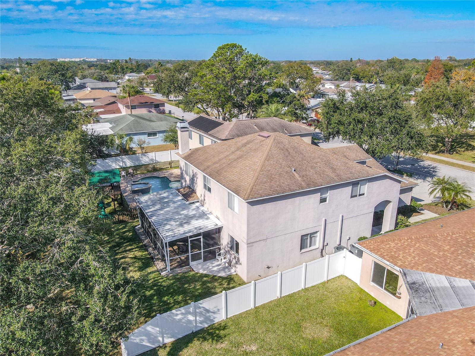Aerial view showcases the home’s expansive screened lanai and fully fenced backyard, offering great outdoor living space with mature trees and a peaceful neighborhood setting.
