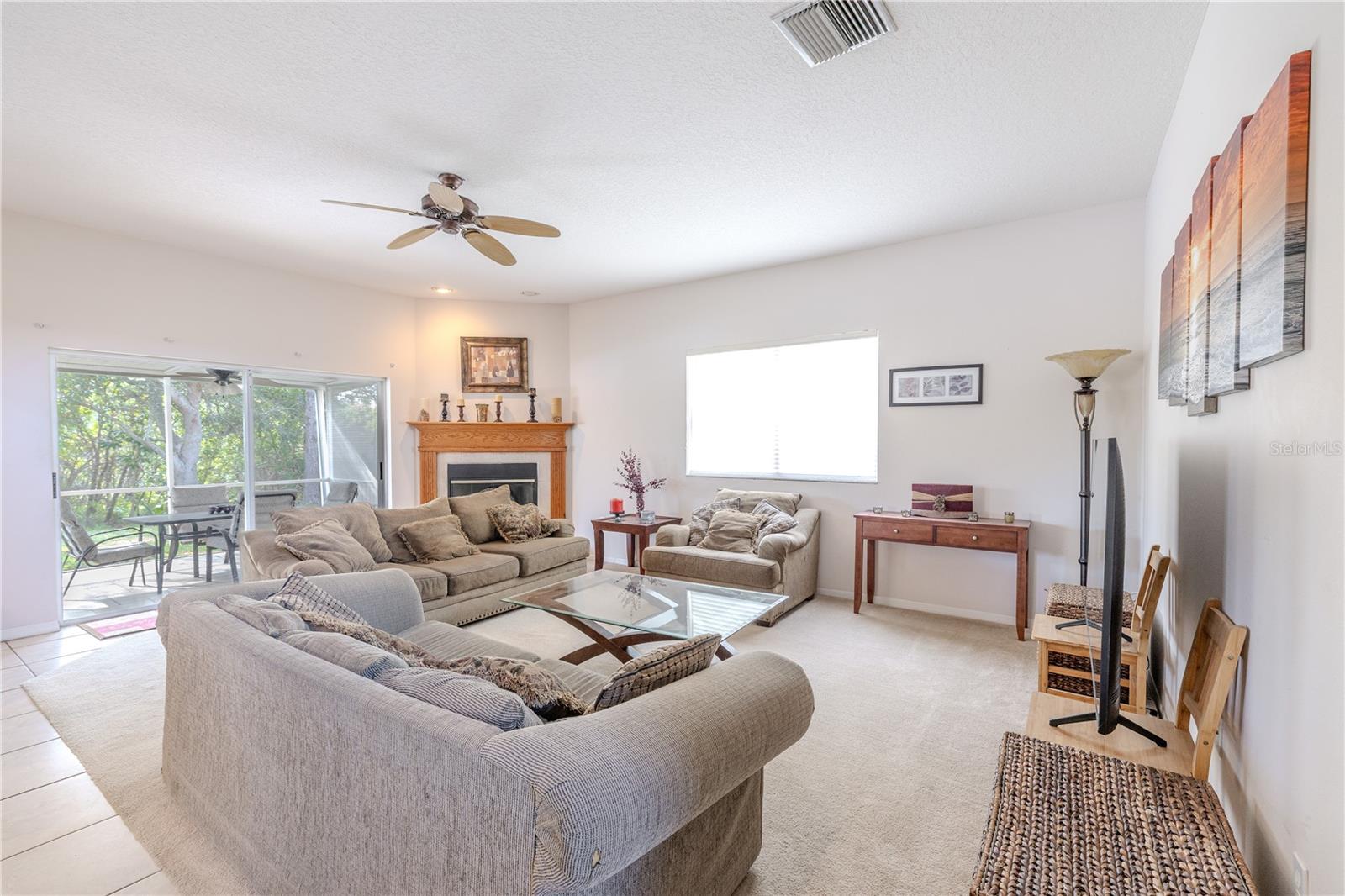 Light-filled family room features a cozy wood-mantle fireplace, generous seating space, and sliding glass doors that open to the screened lanai for effortless indoor-outdoor living.