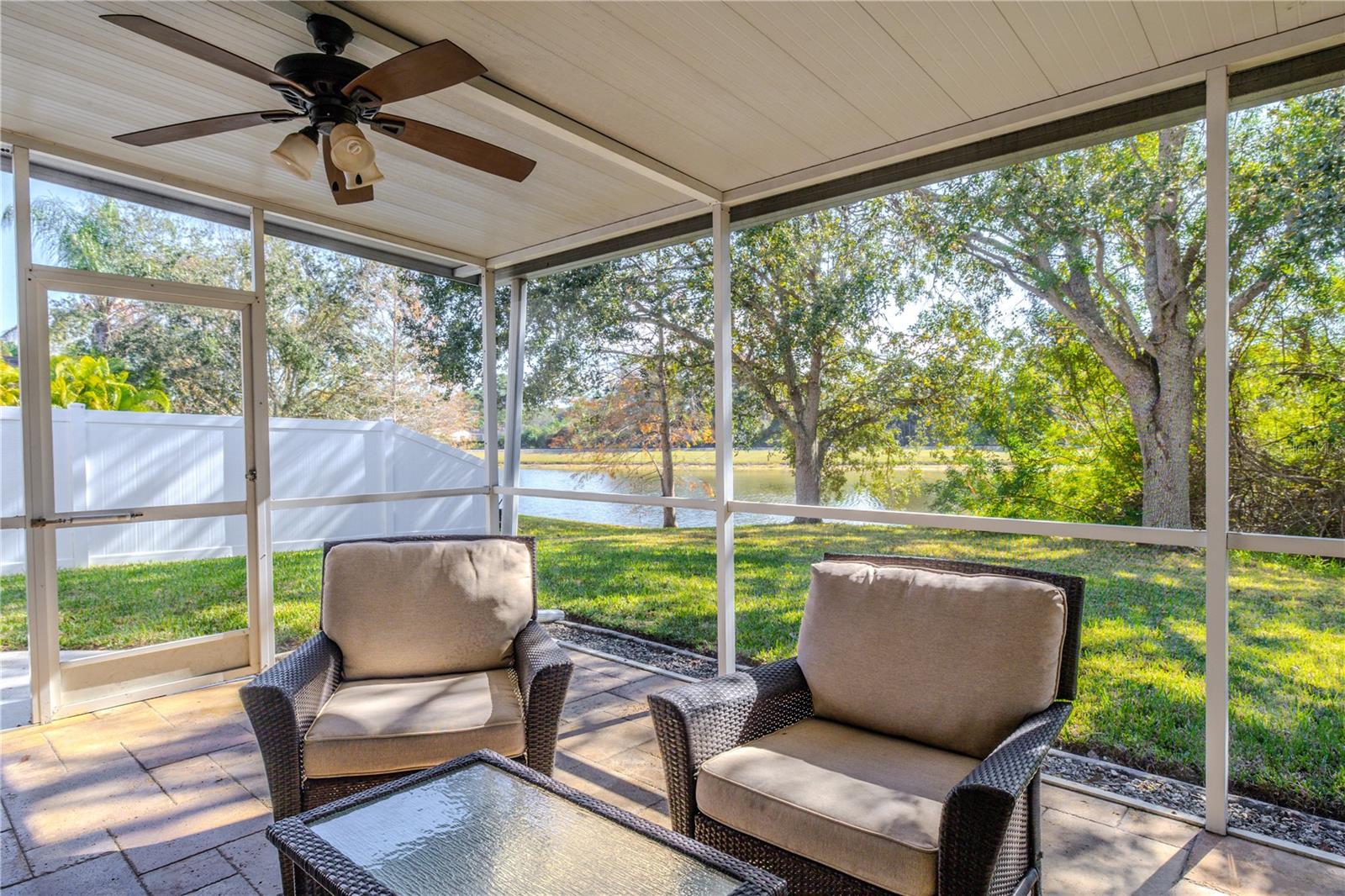 Unwind on the screened lanai with a ceiling fans, comfortable seating, and tranquil pond views framed by mature trees and a spacious backyard.