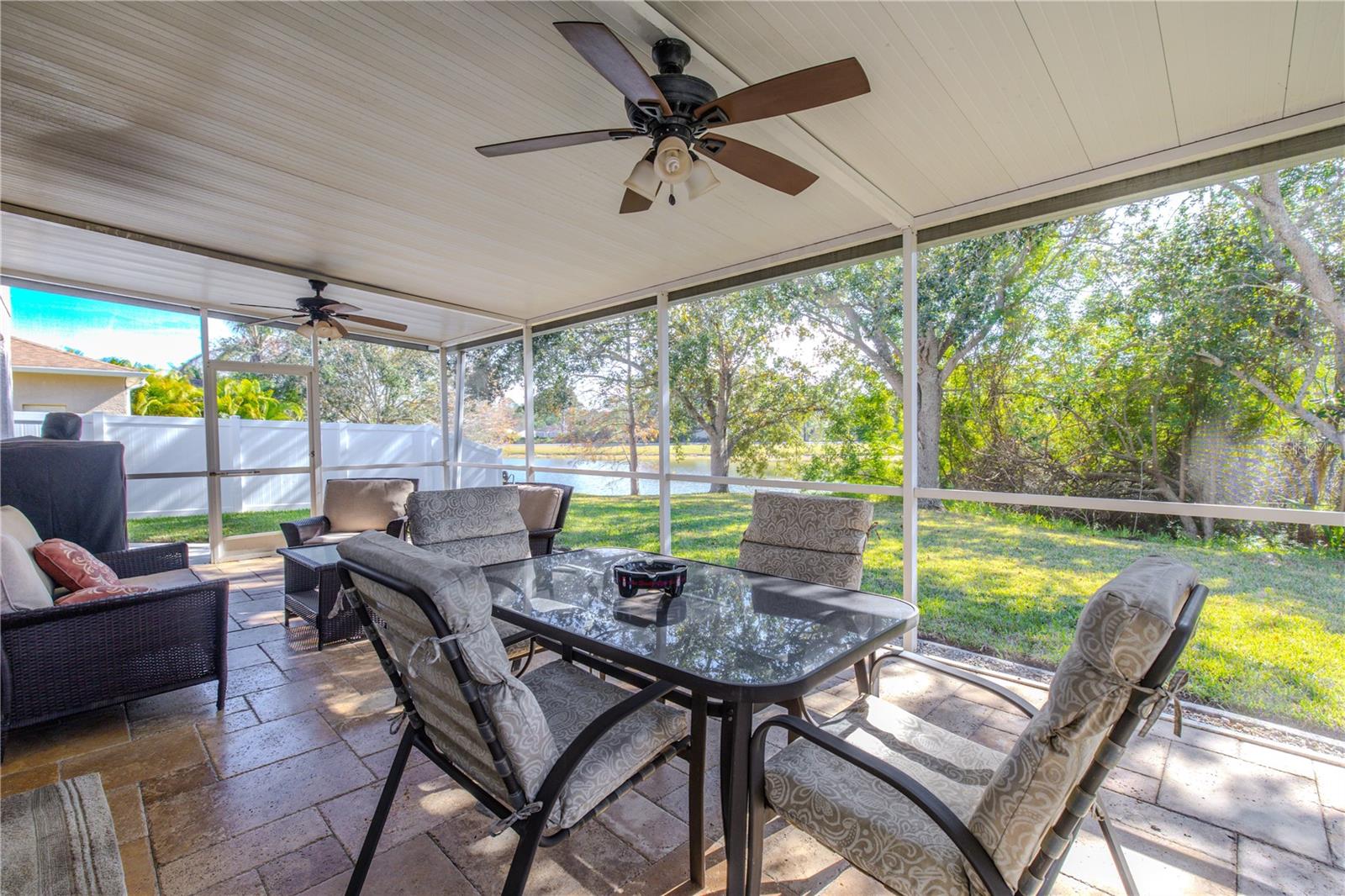 Spacious screened lanai with ceiling fans and an outdoor dining area overlooks the lush backyard and peaceful pond—perfect for entertaining or relaxing year-round.