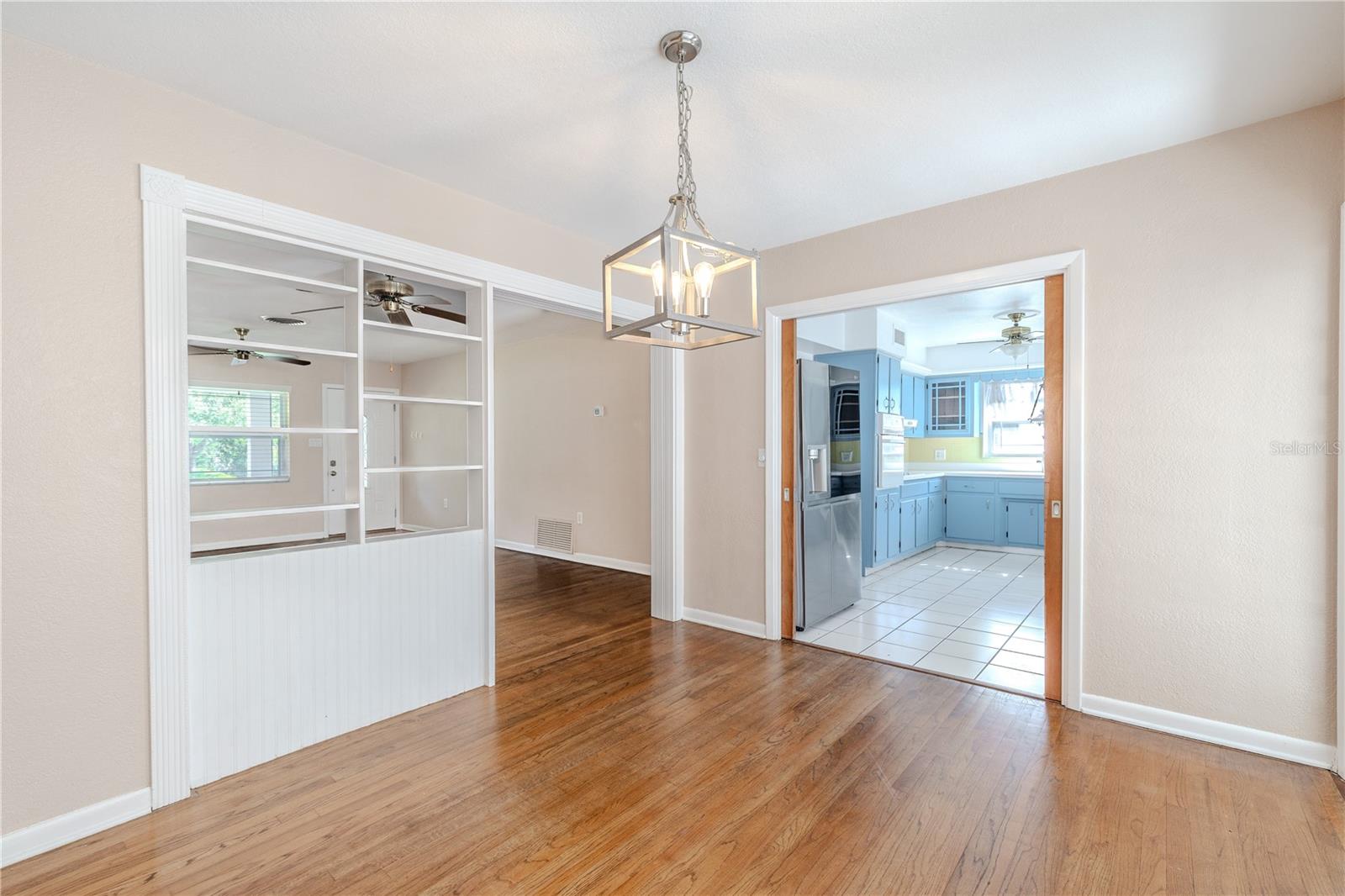 Hardwood floor dining room with a modern pendant light, featuring built-in display shelving and an easy flow into the kitchen and main living area.