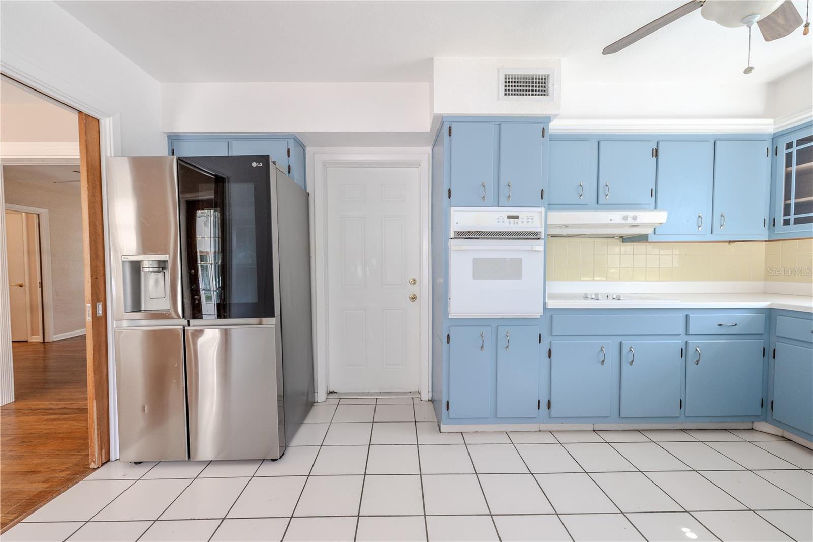 Kitchen view showcasing the convenient garage-entry door, with tile flooring, classic solid wood blue cabinetry, and a stainless refrigerator for everyday functionality.