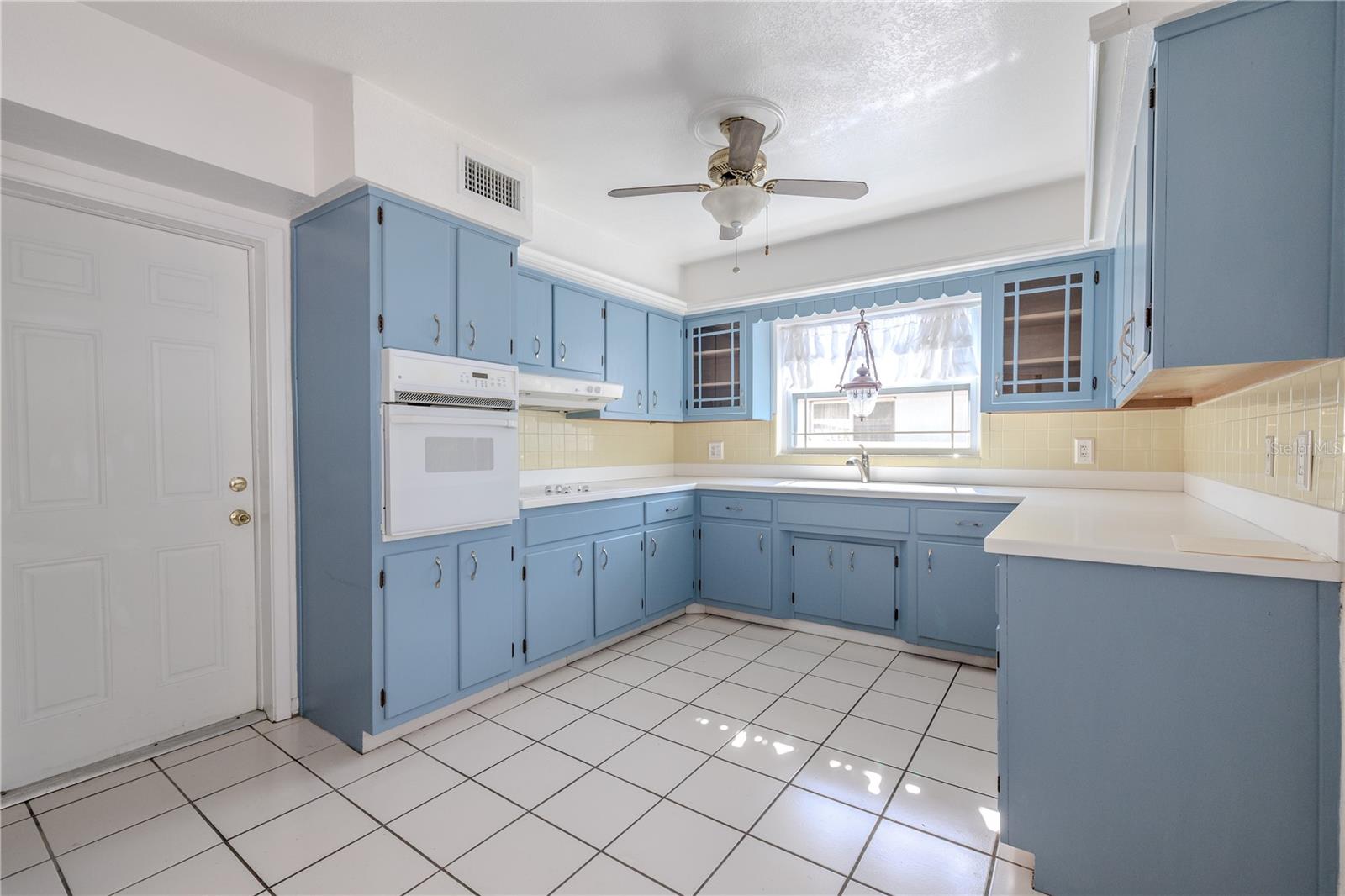 Additional view of the bright, spacious eat in kitchen with charming solid wood blue cabinetry, abundant counter and storage space, tile flooring, and a stainless refrigerator, centered around a window over the sink for natural light.