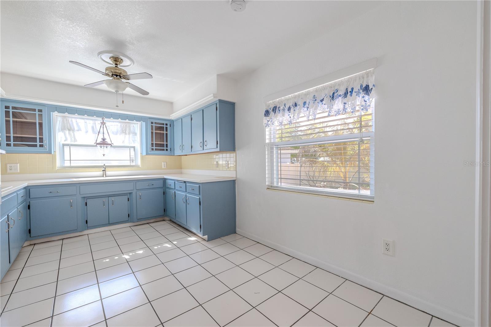 Additional view of the bright, spacious eat in kitchen with charming solid wood blue cabinetry, abundant counter and storage space, tile flooring, and a stainless refrigerator, centered around a window over the sink for natural light.