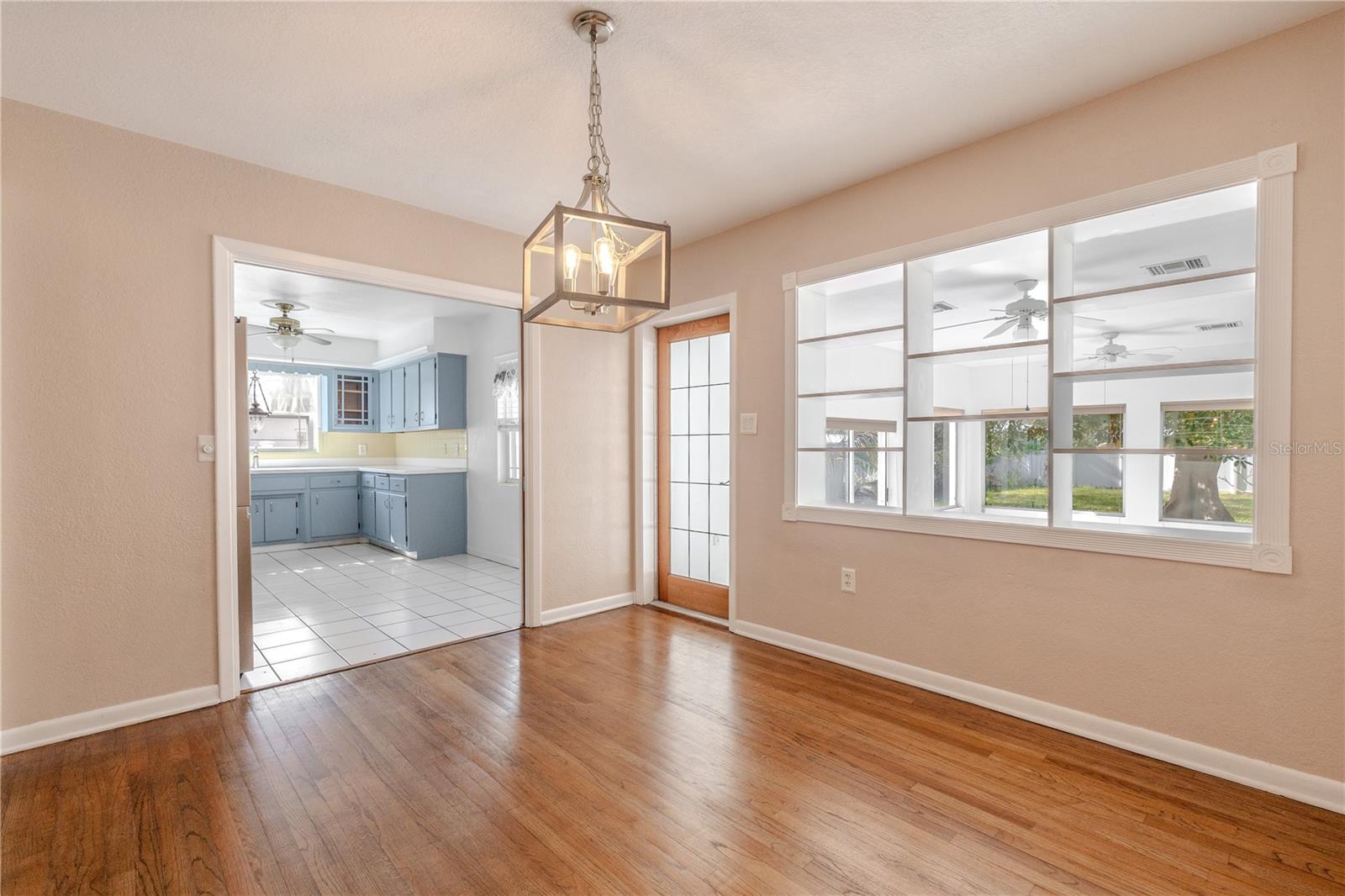 Bright dining area with hardwood floors and a modern pendant light, featuring a glass panel entry door to the Florida room and stylish interior built in shelves with open sight lines to the Florida room.