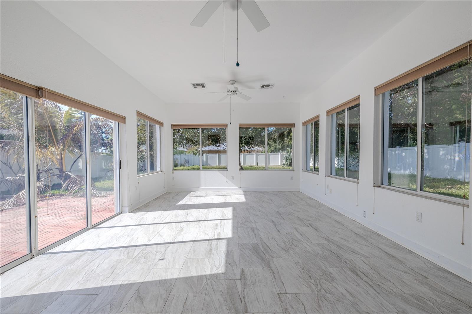 Expansive, light-filled Florida room with walls of windows, ceilings fans, and gorgeous tile flooring, plus sliding doors that open to the brick paver patio and fenced backyard.
