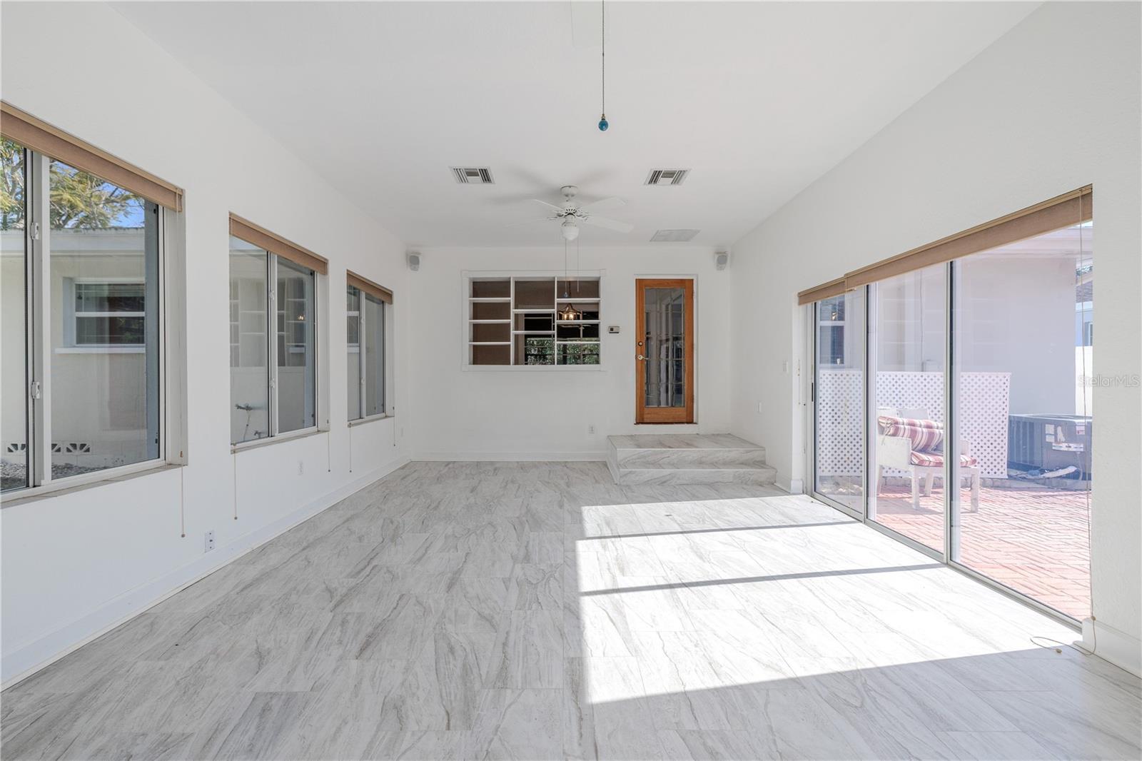 Additional view of the expansive, light-filled Florida room with walls of windows, ceilings fans, and gorgeous tile flooring, plus sliding doors that open to the brick paver patio and fenced backyard.