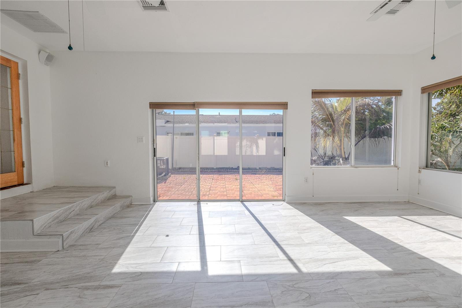 Side view, of the light-filled Florida room with walls of windows, ceilings fans, and gorgeous tile flooring, plus sliding doors that open to the brick paver patio and fenced backyard.