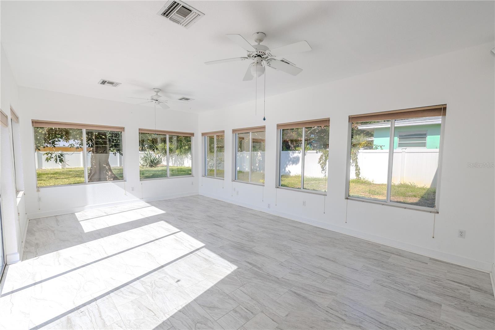 Additional view of the expansive, light-filled Florida room with walls of windows, ceilings fans, and gorgeous tile flooring, plus sliding doors that open to the brick paver patio and fenced backyard.