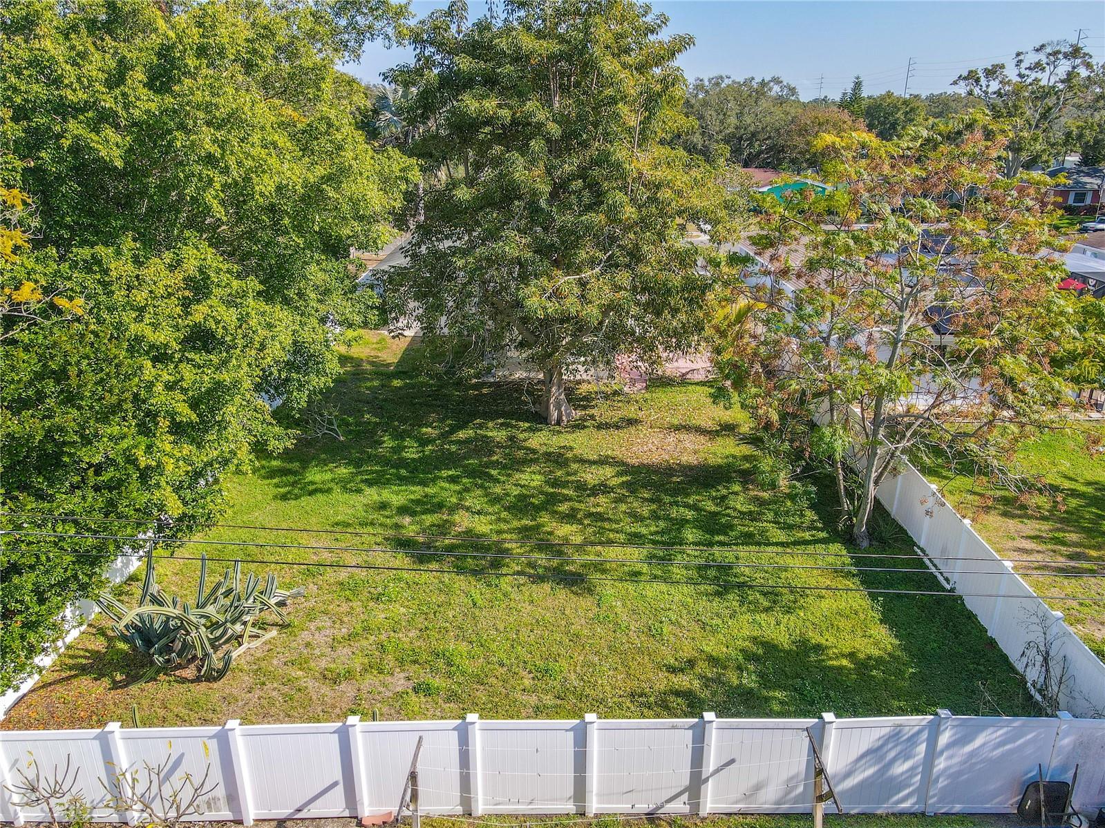 Aerial view of the spacious fenced backyard with mature shade trees and plenty of open green space—perfect for outdoor entertaining, pets, or a future garden oasis.