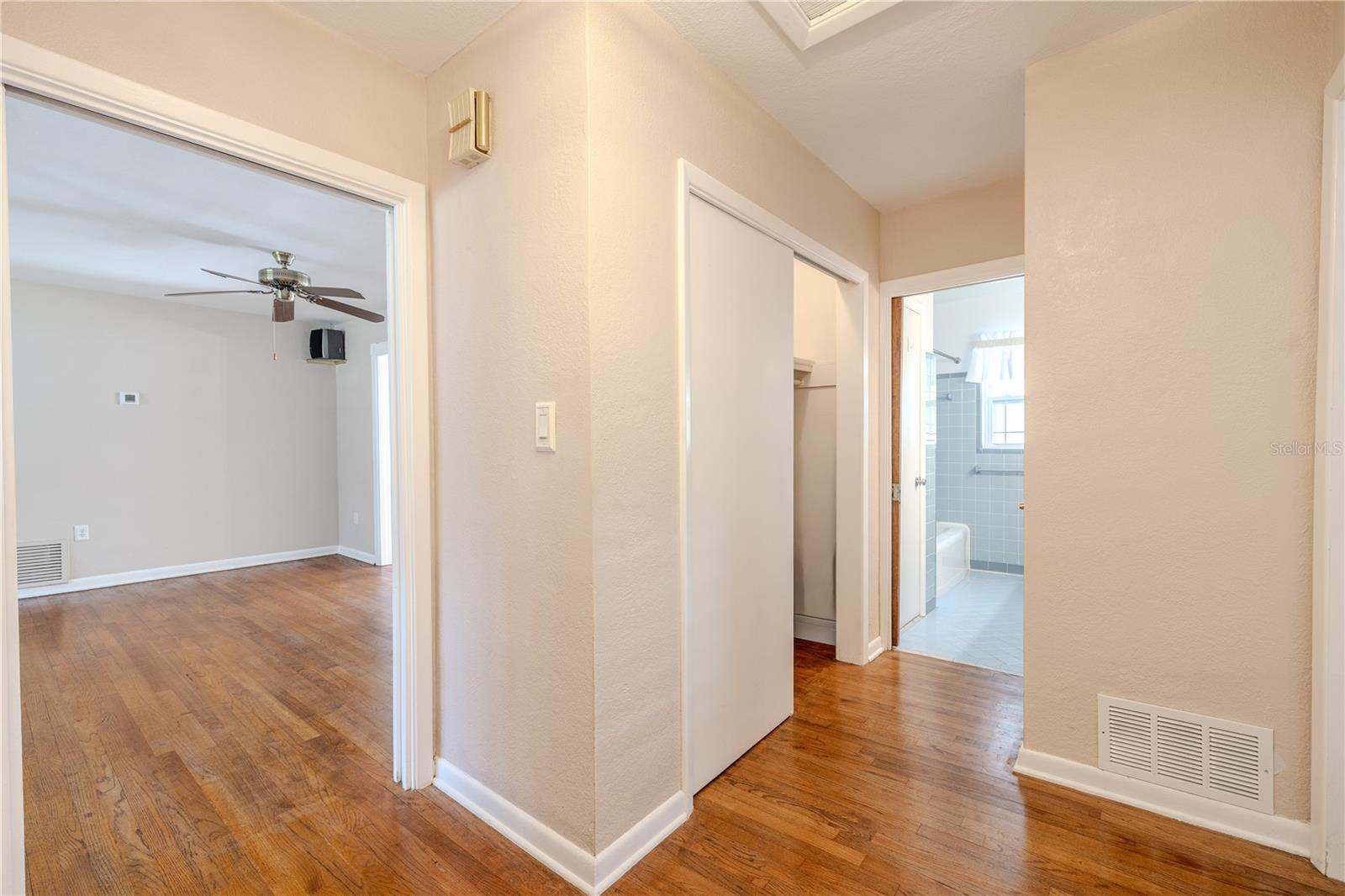 Hallway view showing the bedroom wing with hardwood floors, a convenient clothes closet, and easy access to the full bath, with the living area just beyond.