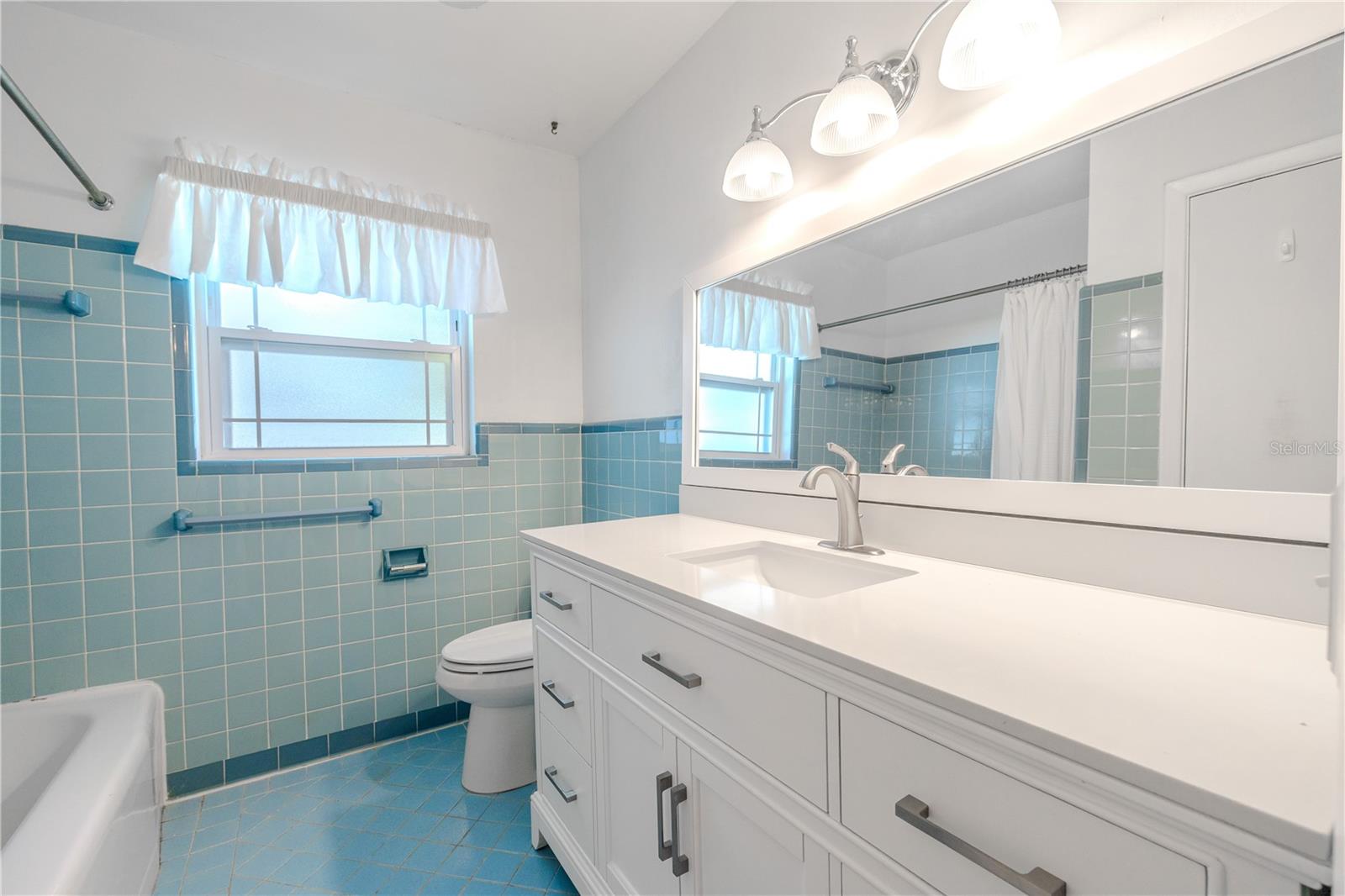 Bright full second bathroom featuring a long updated vanity with generous storage, built in linen closet, classic tile work, and a tub/shower combo with a privacy window for natural light.