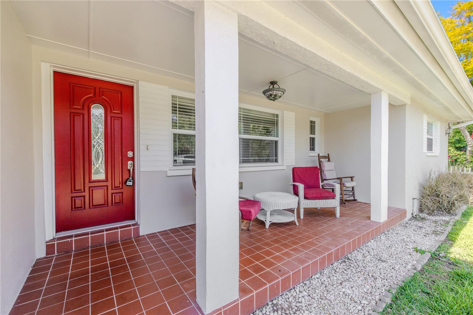 Inviting covered front porch with classic tile flooring, seating space for relaxing, and a striking red front door that adds charming curb appeal.