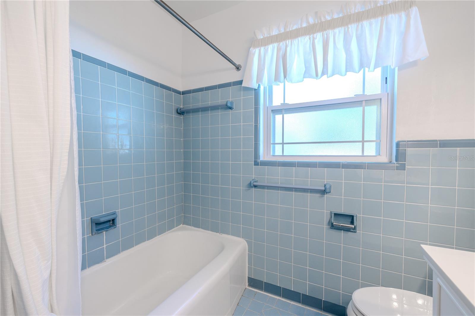 Additional view of the bright right full second bathroom featuring a long updated vanity with generous storage, built in linen closet, classic tile work, and a tub/shower combo with a privacy window for natural light.