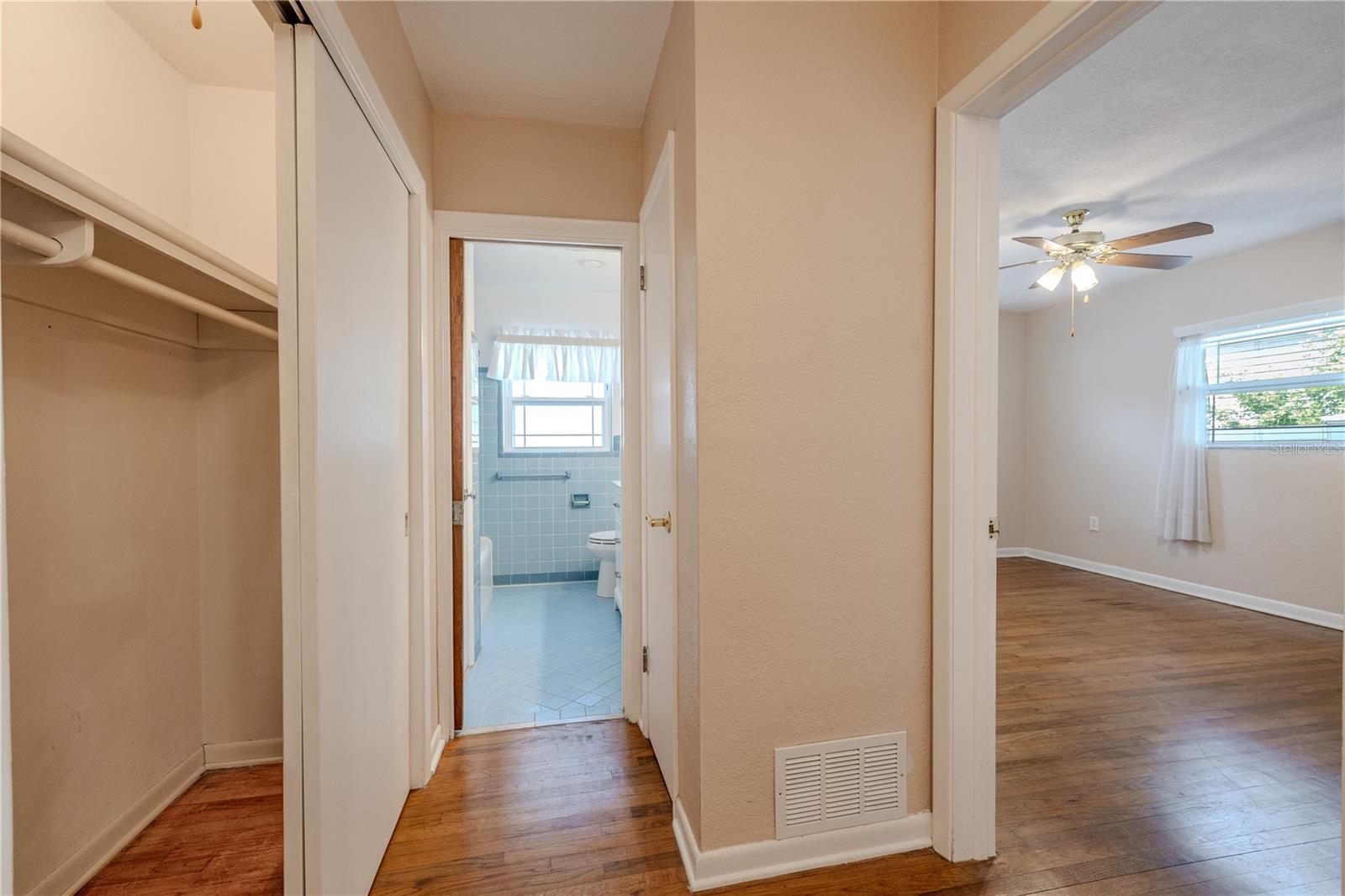 Hallway view with a convenient closet and easy access to the full bath, plus a look into a spacious bedroom with hardwood floors, ceiling fan, and natural light.