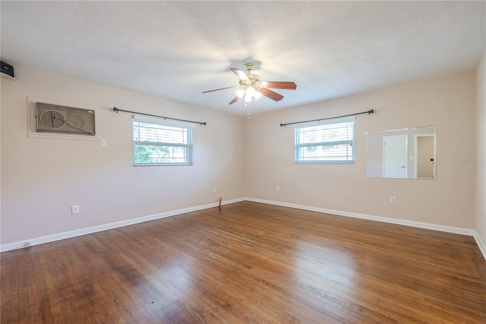 Spacious primary bedroom, en-suite bathroom, with hardwood floors, ceiling fan, and dual windows that bring in abundant natural light for a bright, comfortable retreat.