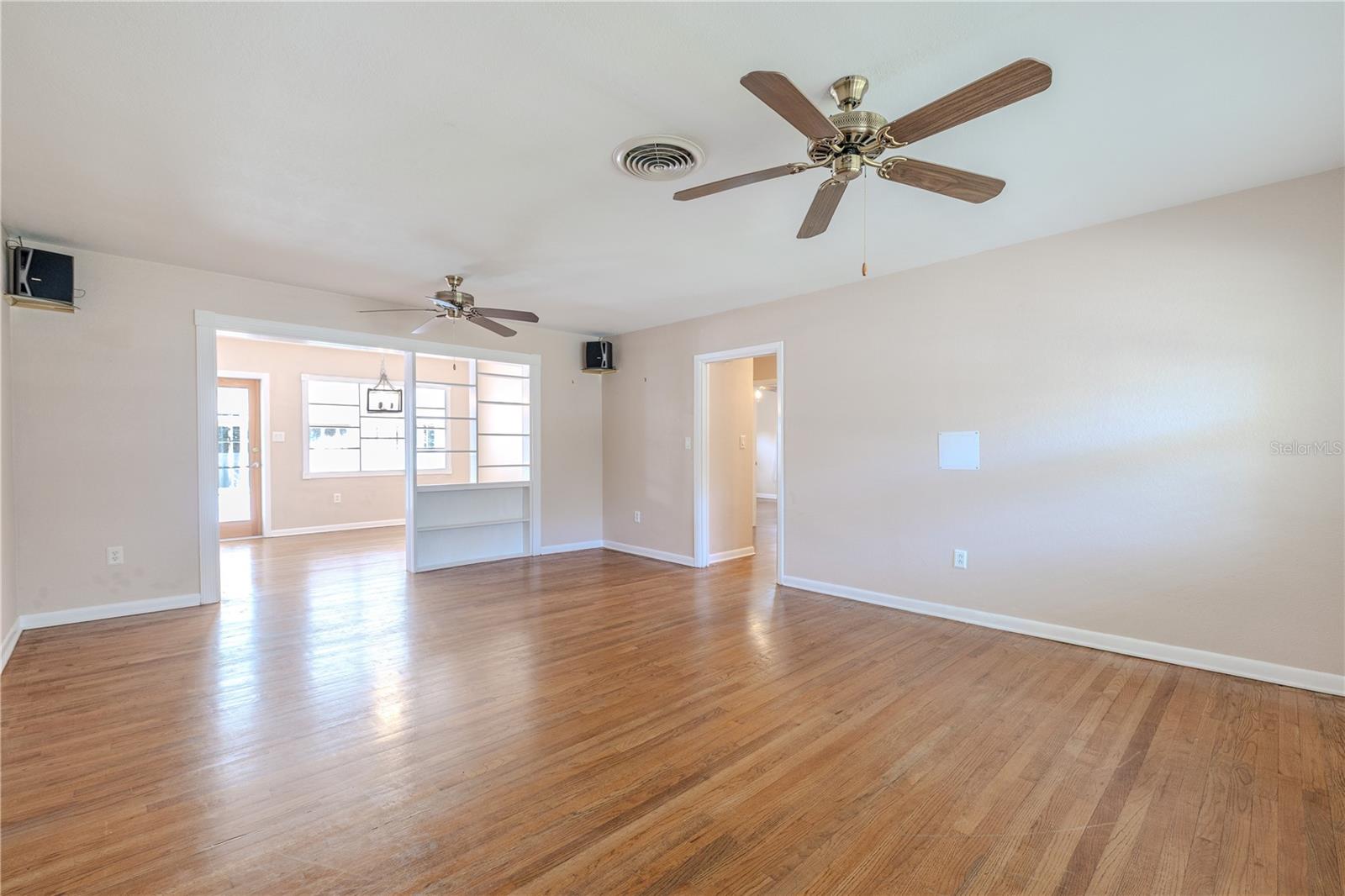 Spacious main living area with gleaming hardwood floors, ceiling fans, and an open flow into the dining room and Florida room for flexible living and entertaining.