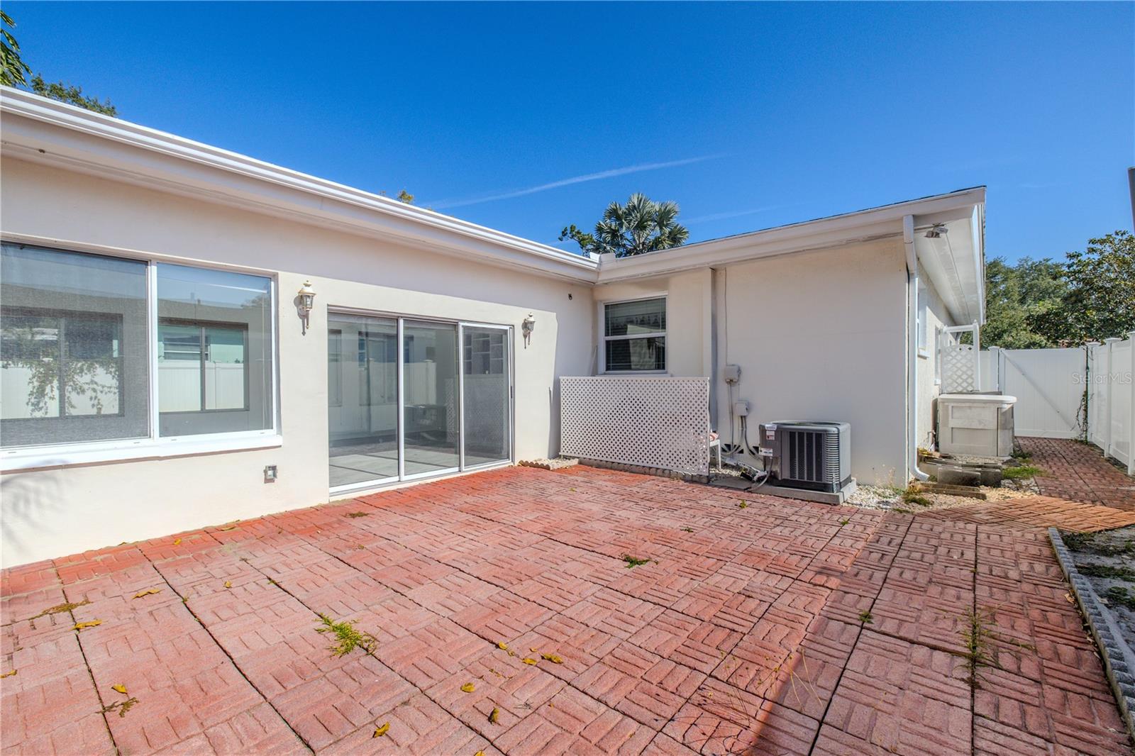 Additional view of the spacious brick paver patio off the Florida room, offering easy indoor-outdoor living with sliding glass doors, mature shade trees, and a fenced backyard for privacy.