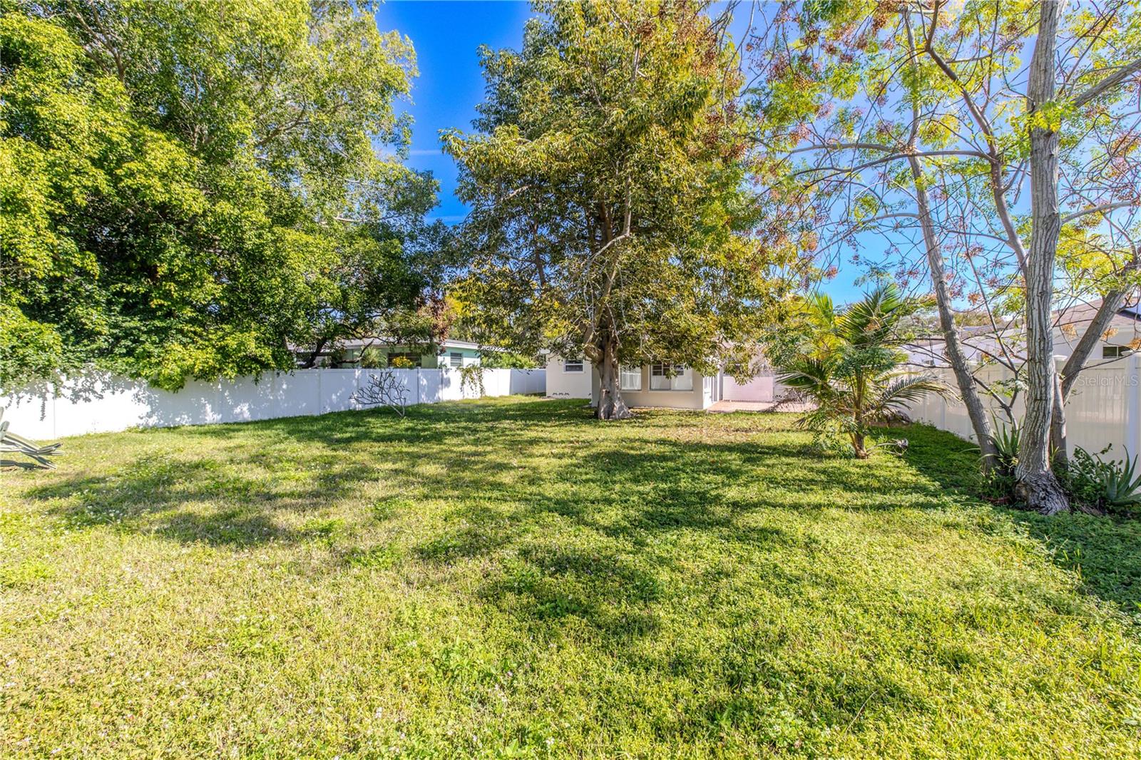 Additional view of the spacious fenced backyard with mature shade trees and plenty of open green space—perfect for outdoor entertaining, pets, or a future garden oasis.