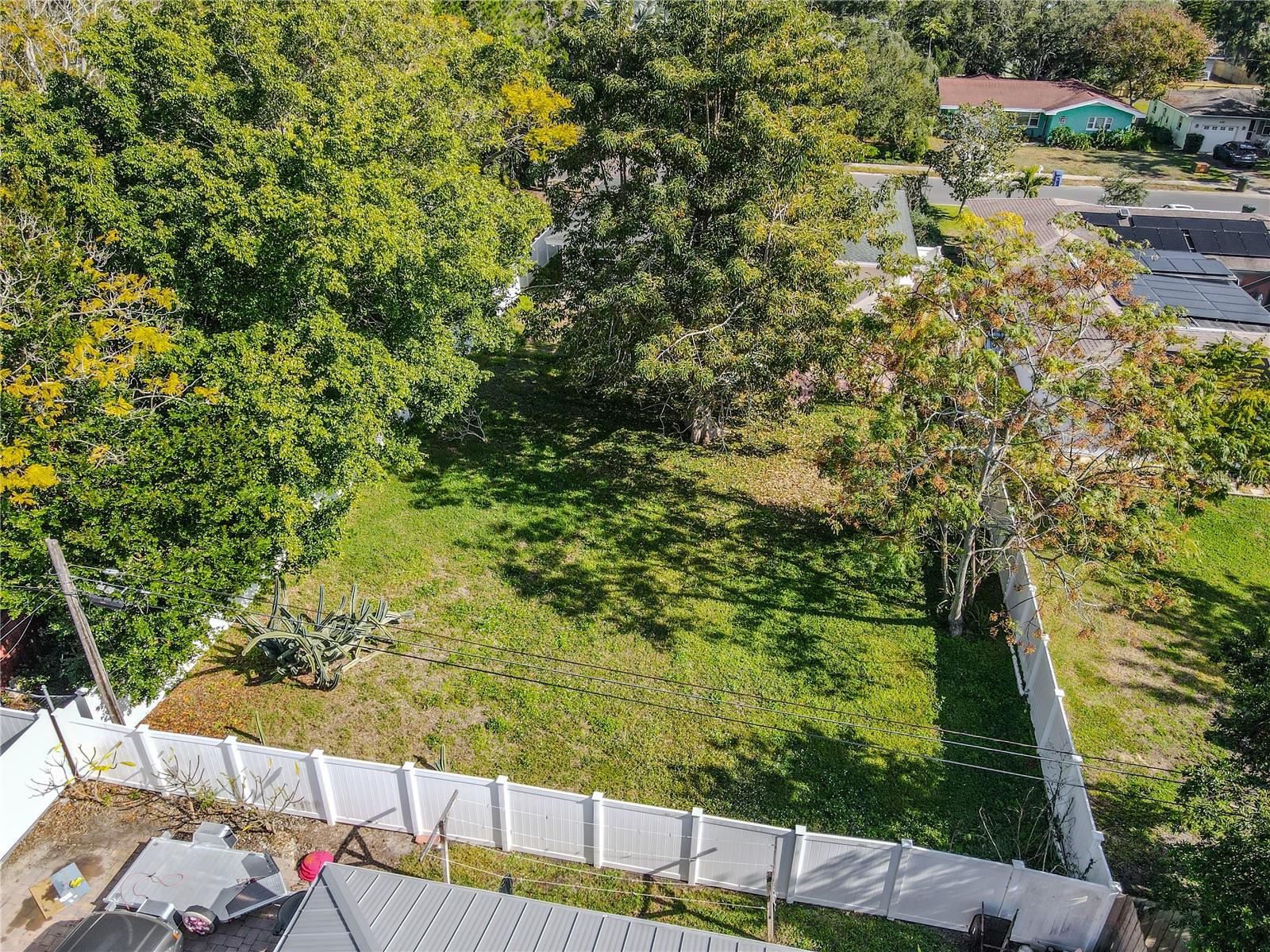Aerial view of the spacious fenced backyard with mature shade trees and plenty of open green space—perfect for outdoor entertaining, pets, or a future garden oasis.