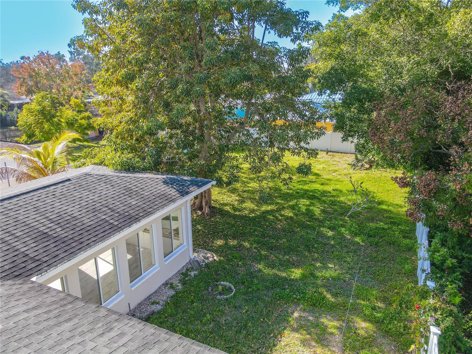 Additional aerial view of the spacious fenced backyard with mature shade trees and plenty of open green space—perfect for outdoor entertaining, pets, or a future garden oasis.