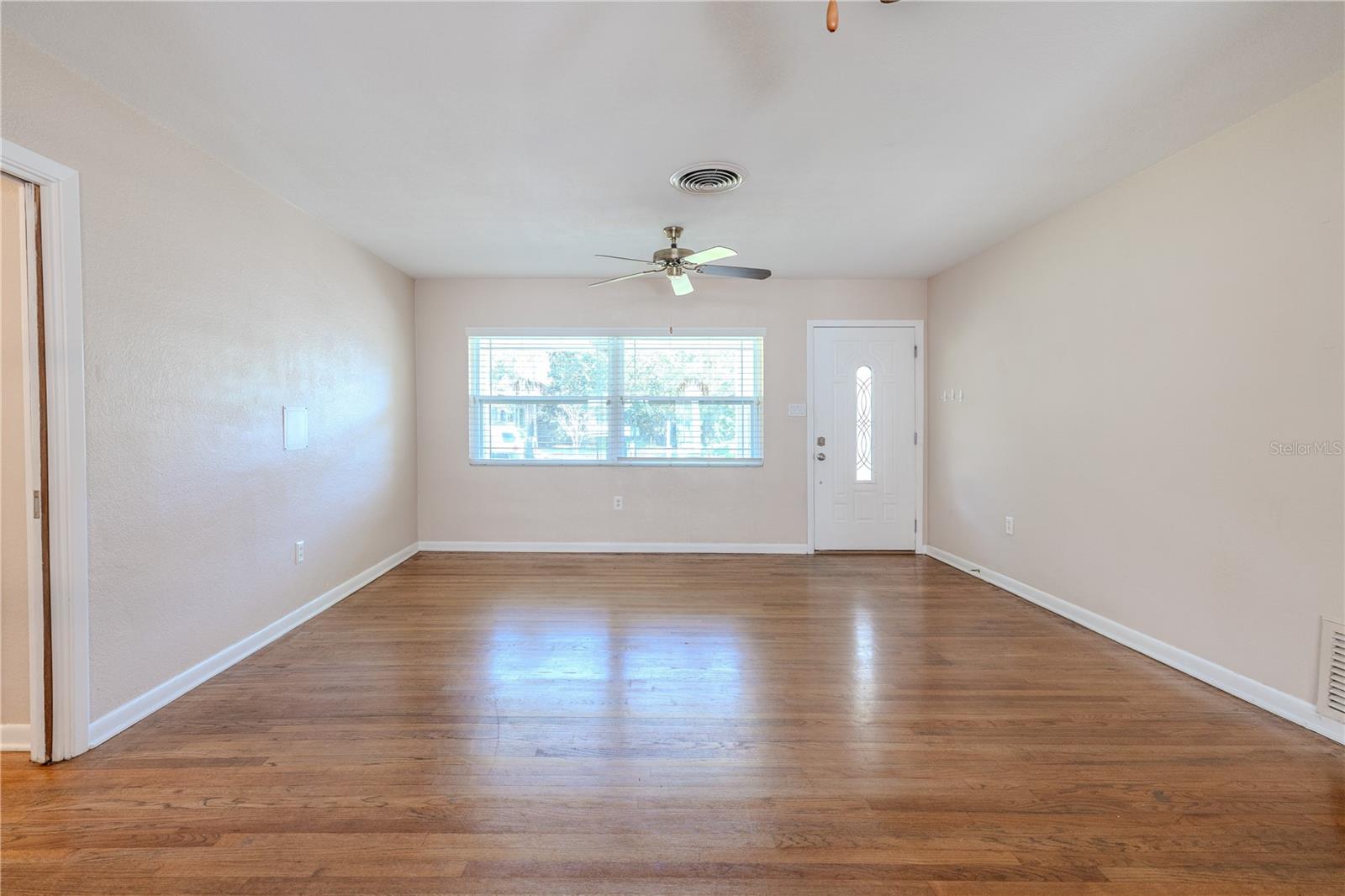 Bright living room with beautiful hardwood floors, a ceiling fans, and a large picture window that fills the space with natural light.