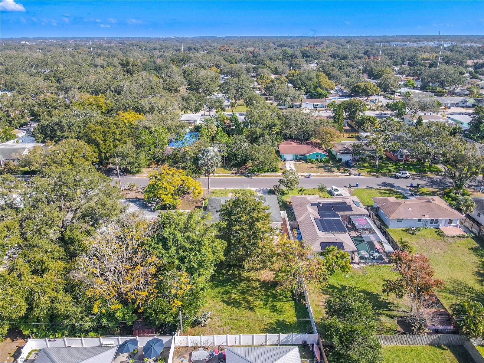 Aerial neighborhood view highlighting the home’s large, tree-lined lot with a spacious fenced backyard, nestled in an established community with abundant greenery and privacy.