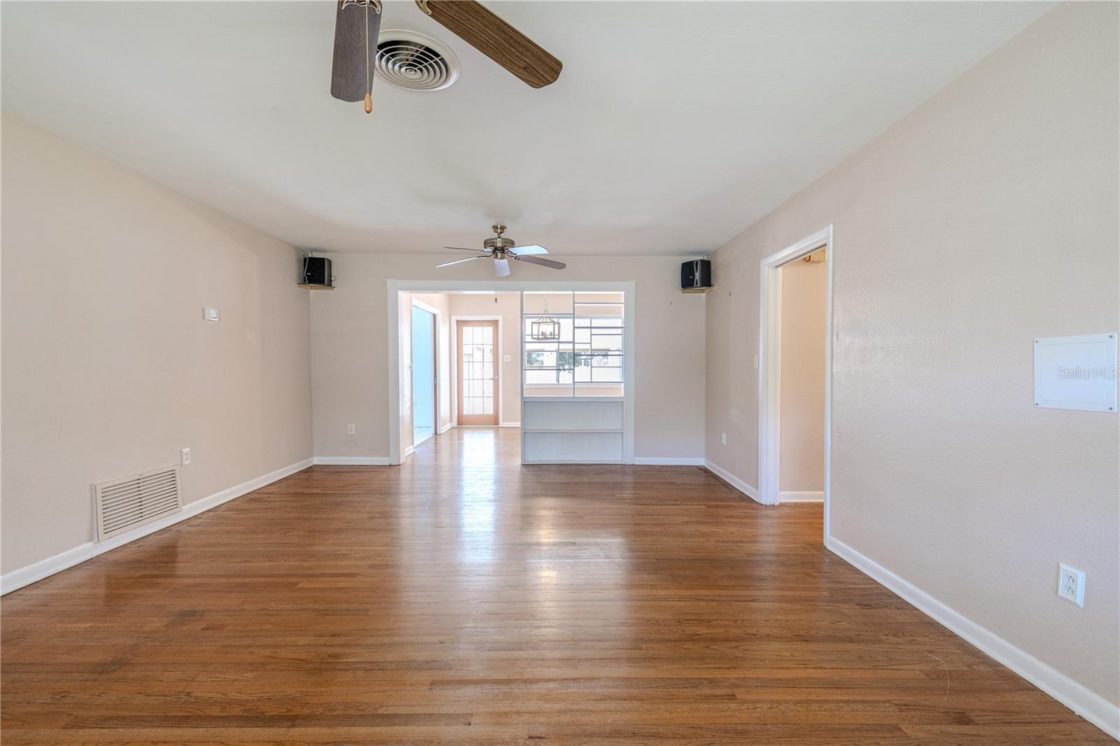 Spacious living room with hardwood floors and ceiling fans, featuring an open flow to the bright dining room, Florida room with built-in shelving and a French pocket doors to the kitchen.