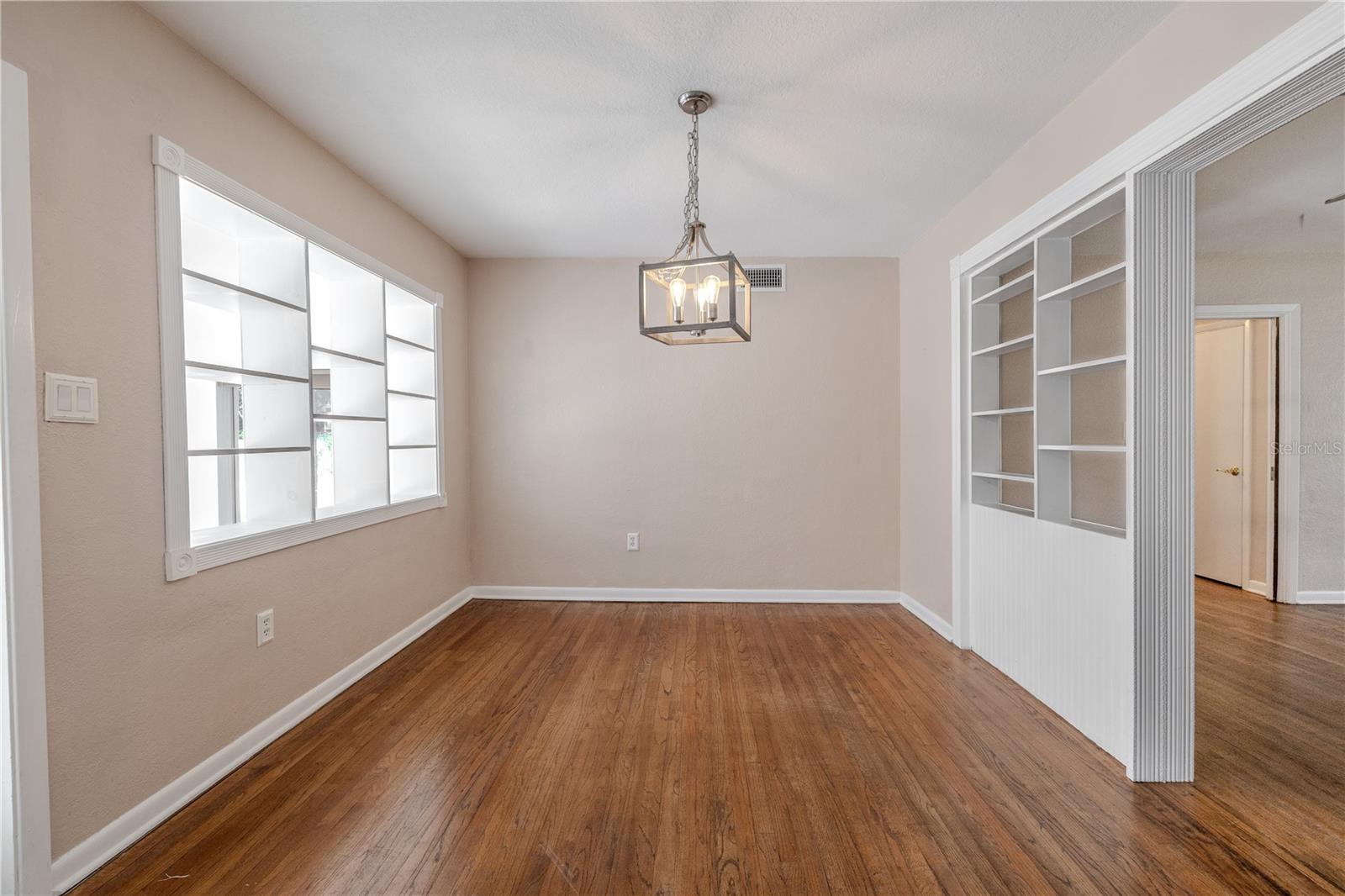 Charming dining room with hardwood floors and a statement pendant light, featuring a decorative interior built in shelves open to the Family room and built-in shelving open to the living room that adds character and function.