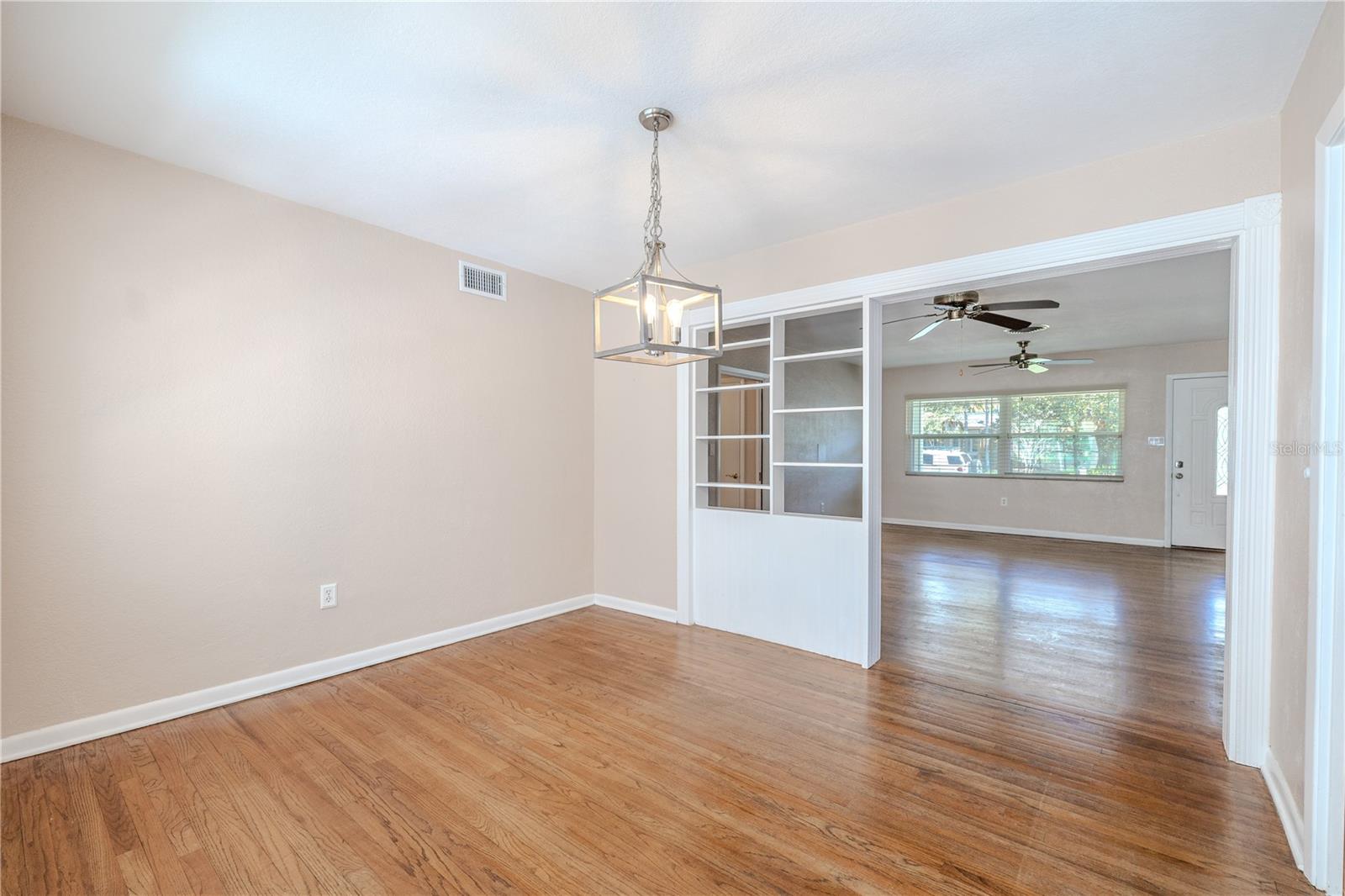 Hardwood floor dining room with a modern pendant light and an open connection to the spacious living area through decorative built-in shelving and interior window details.