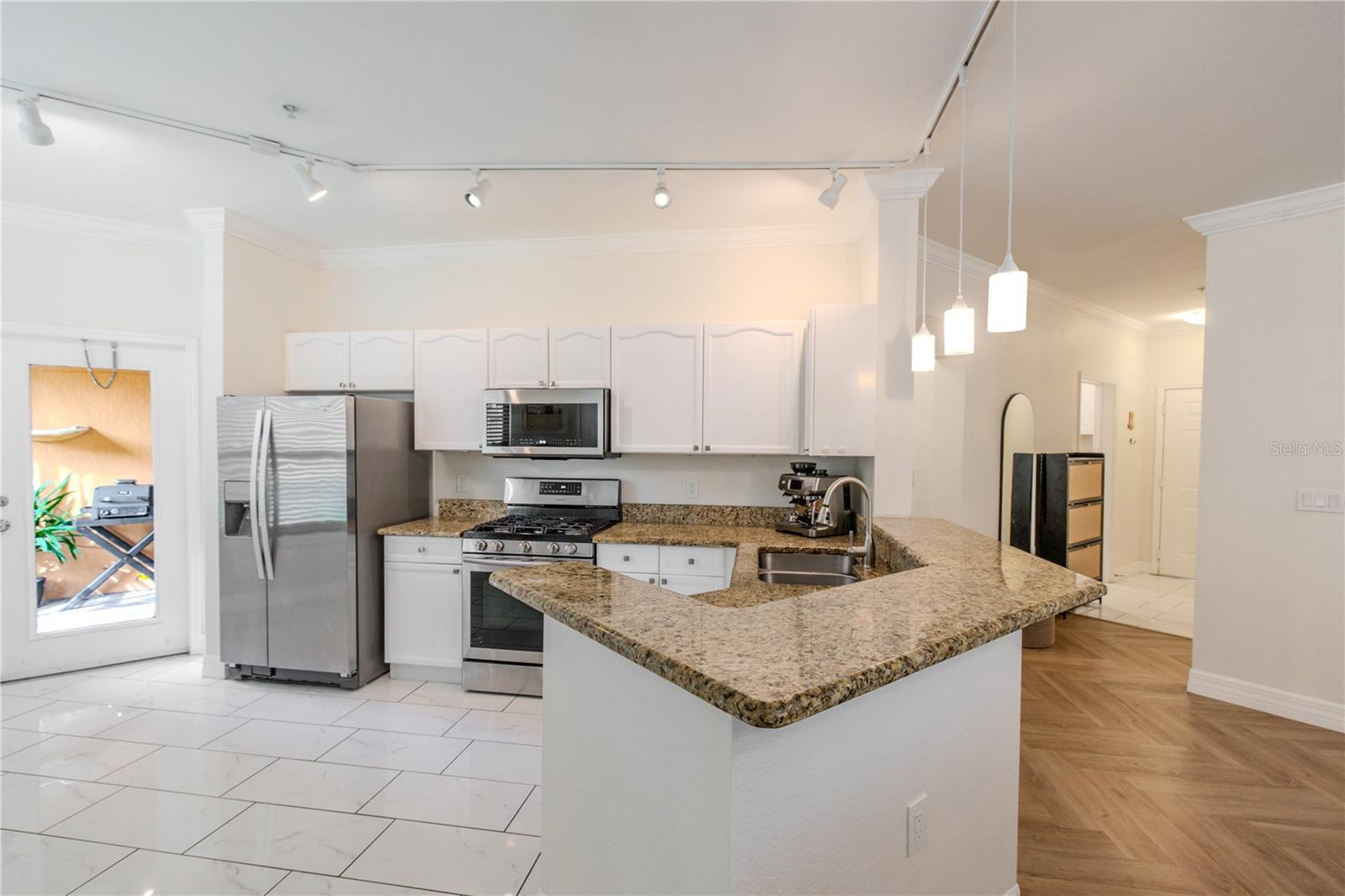 Bright, open kitchen featuring granite countertops, stainless steel appliances, and a spacious peninsula with bar seating and pendant lighting.